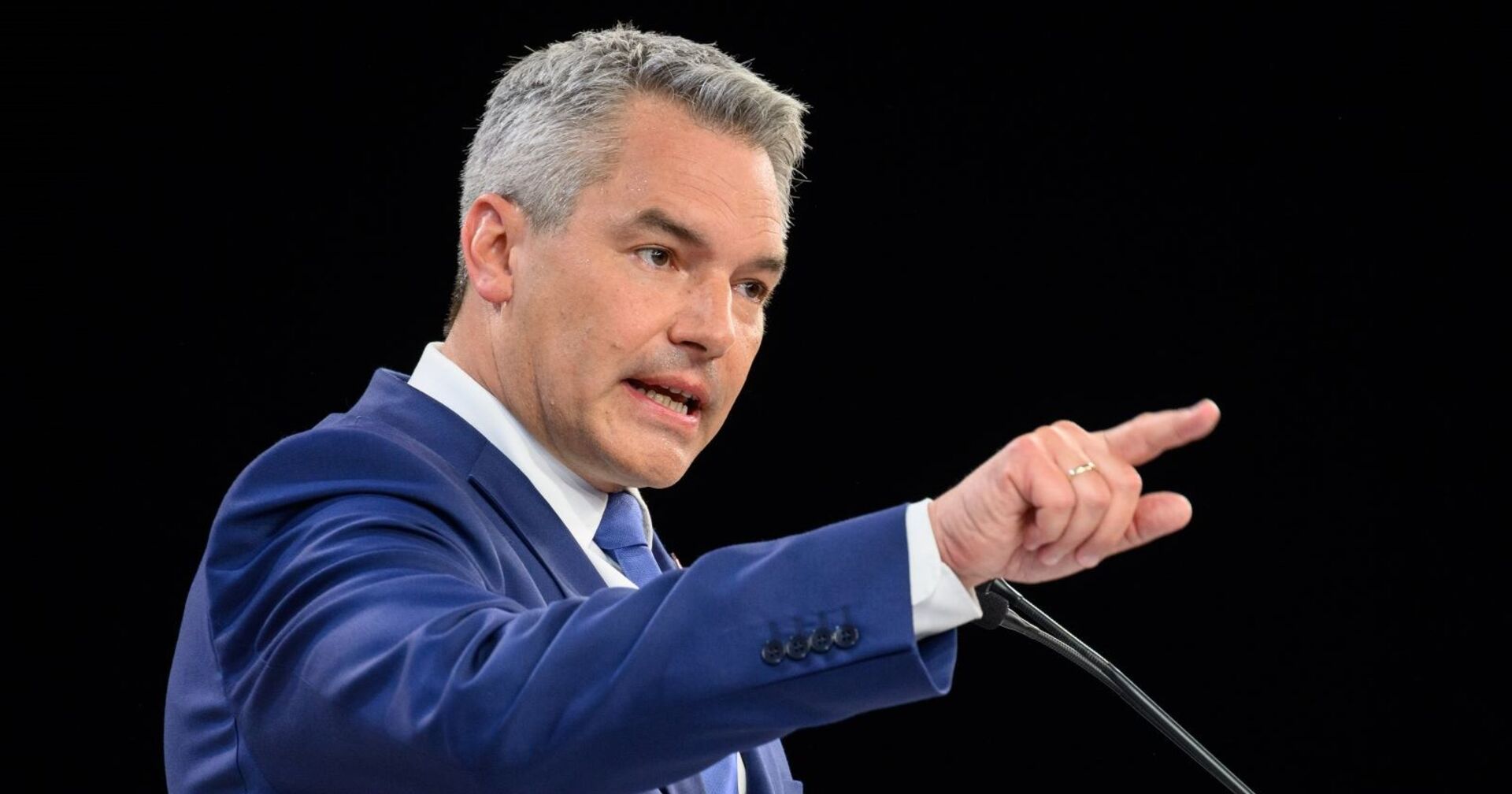 Bundeskanzler Karl Nehammer sprehend am Mikrofon. Er wirkt entschlossen und deutet mit dem Zeigefinger in die Ferne