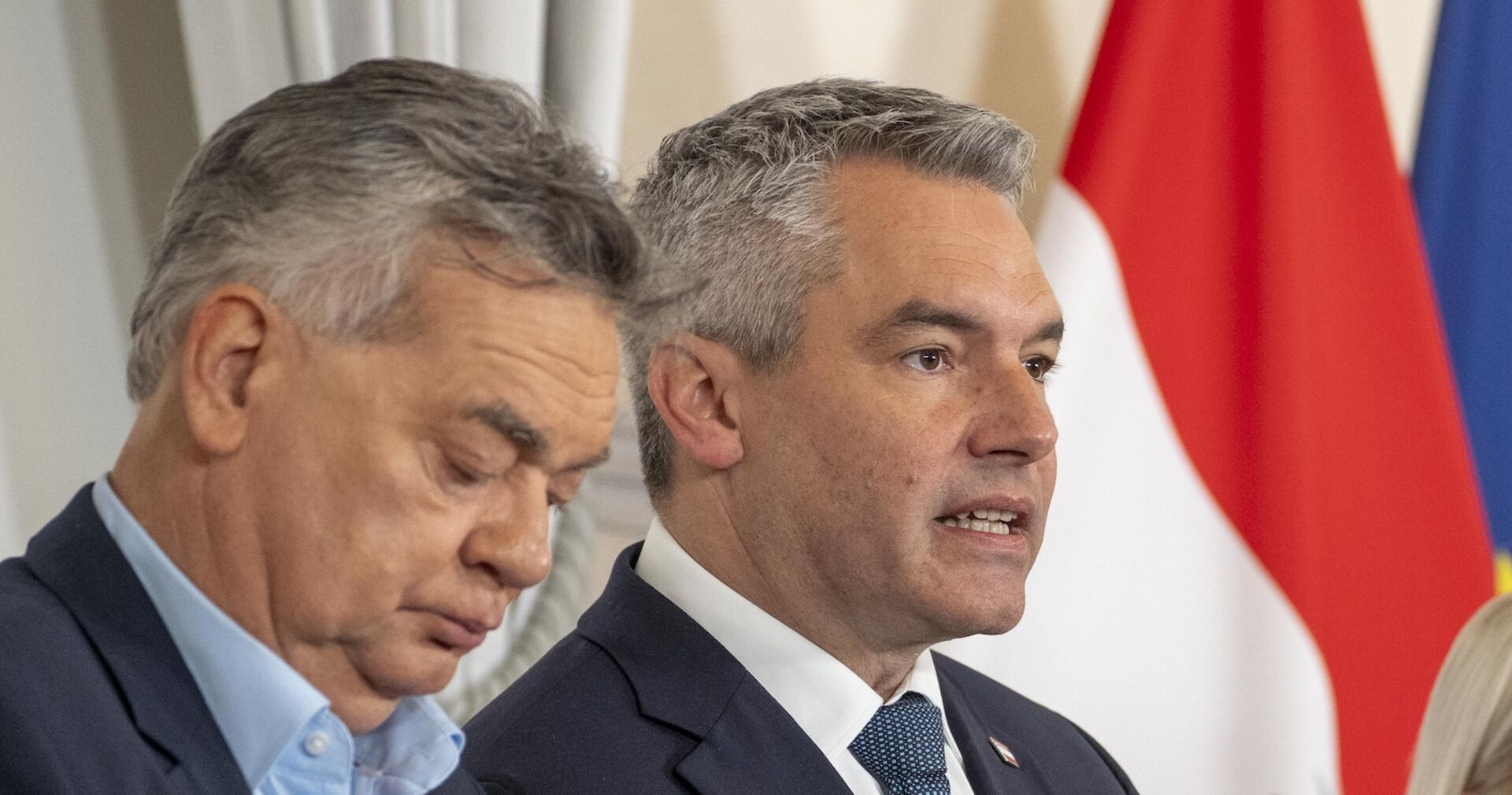 Werner Kogler und Karl Nehammer bei einer Pressekonferenz, im Hintergrund die Flagge Österreichs