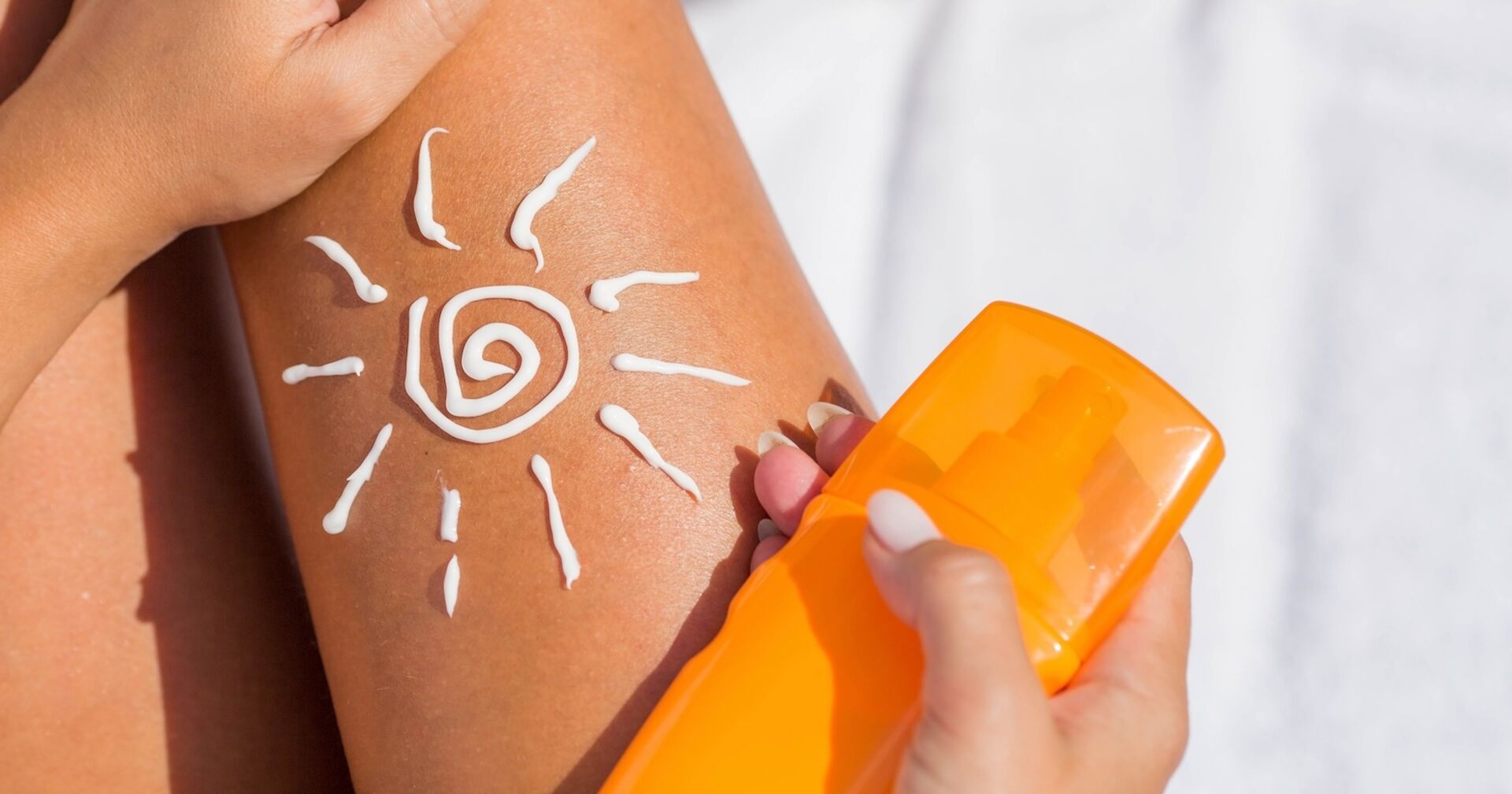 Ein braungebranntes Damenbein, darauf ist aus Sonnencreme eine Sonne gezeichnet, daneben eine Tube Sonnencreme