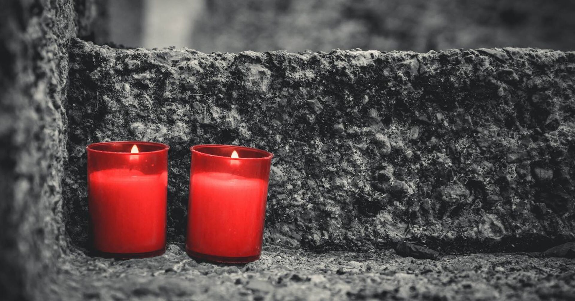 Zwei rote Grabkerzen auf einer Steinstufe.