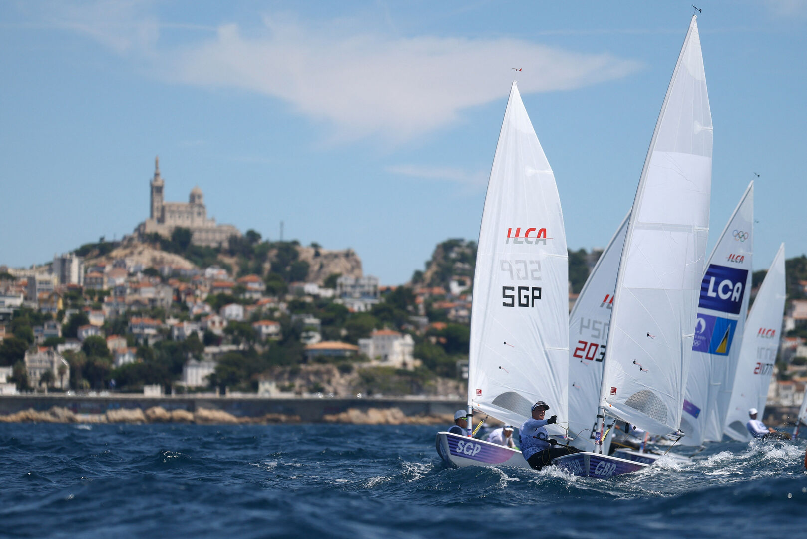 Mehrere Segelboote vor der Küste, dahinter ist eine Stadt zu sehen