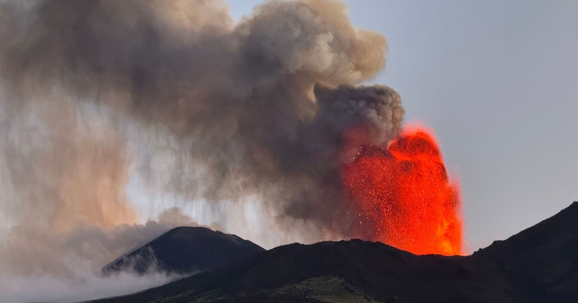 Lava schießt aus dem Krater des Ätnas in die Luft. Eine dicke Rauchsäule steigt auf.