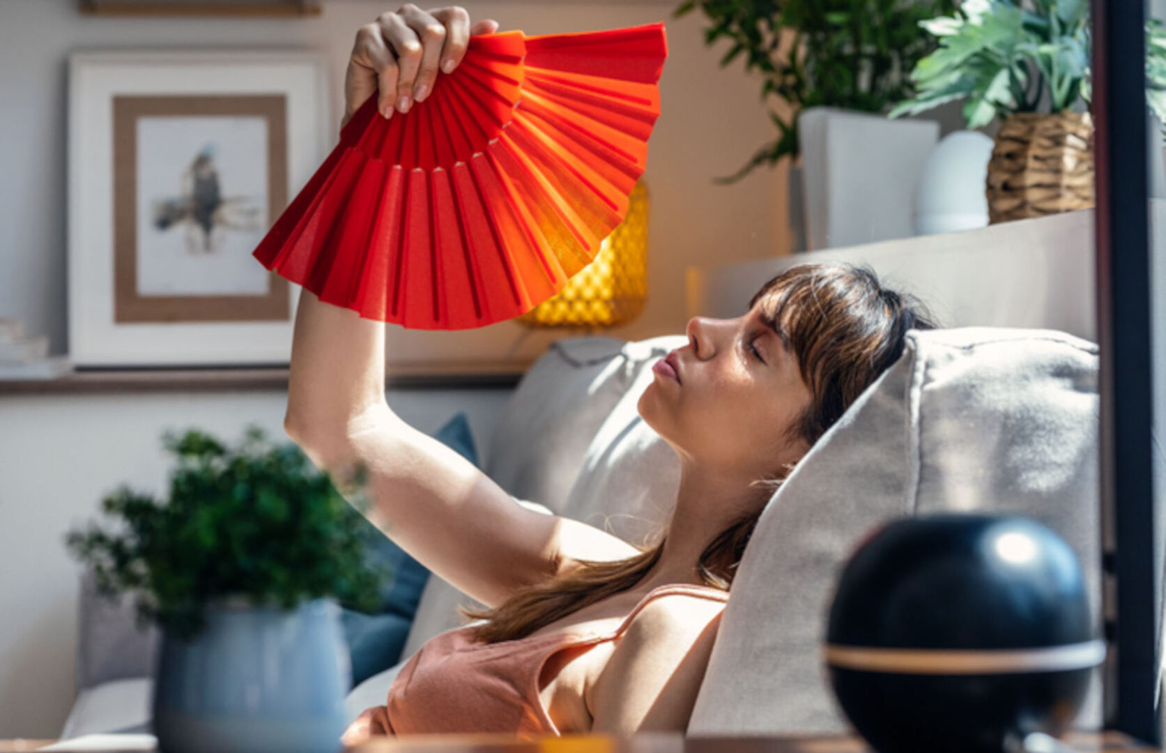 Frau liegt auf einem Sofa und fächelt sich Luft zu