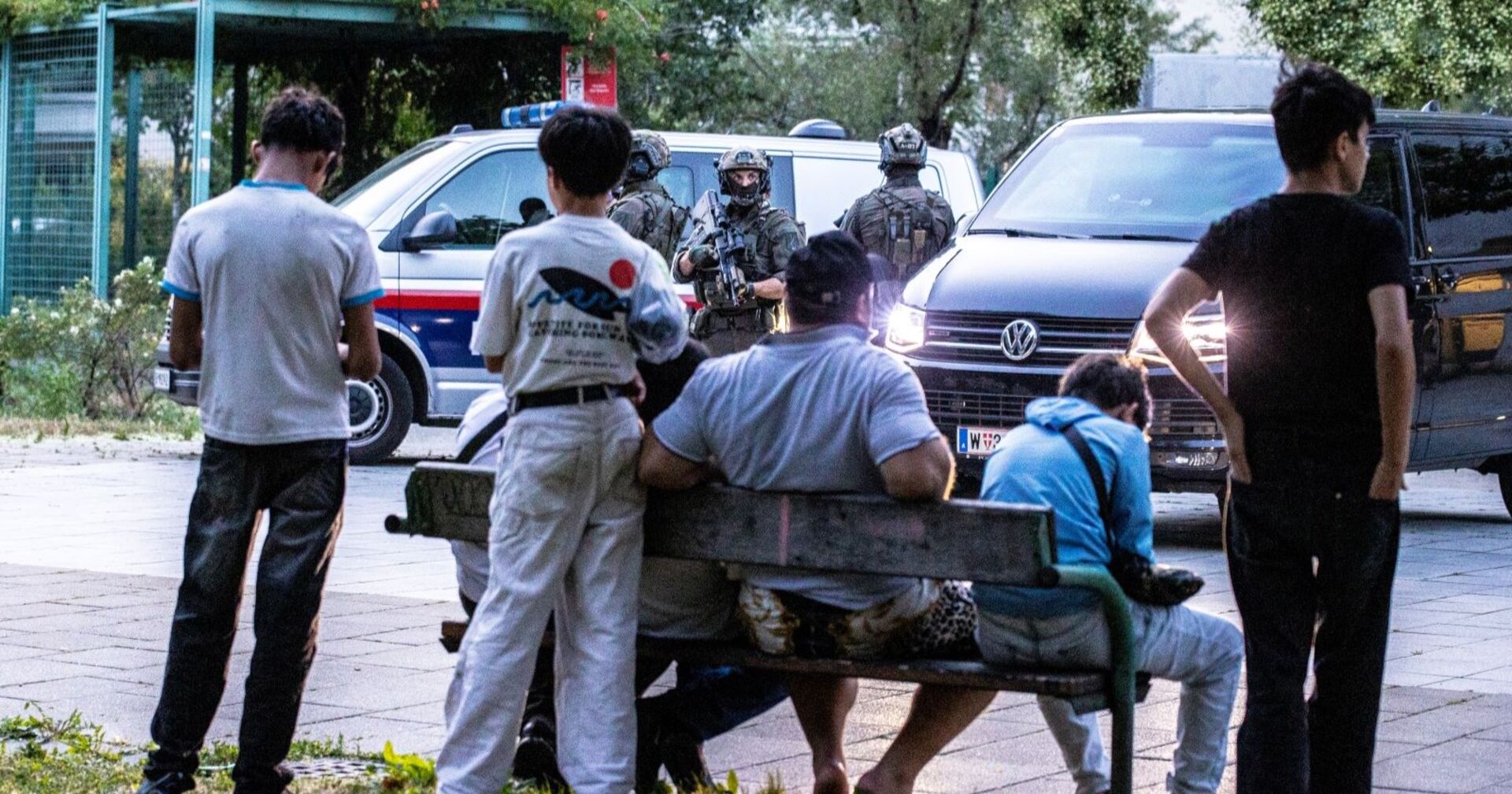 Mehrere Jugendliche um eine Parkbank in einem Wiener Park, sie stehen der schwer bewaffneten Polizei gegenüber, die gerade eine Schwerpunktkontrolle durchführt.
