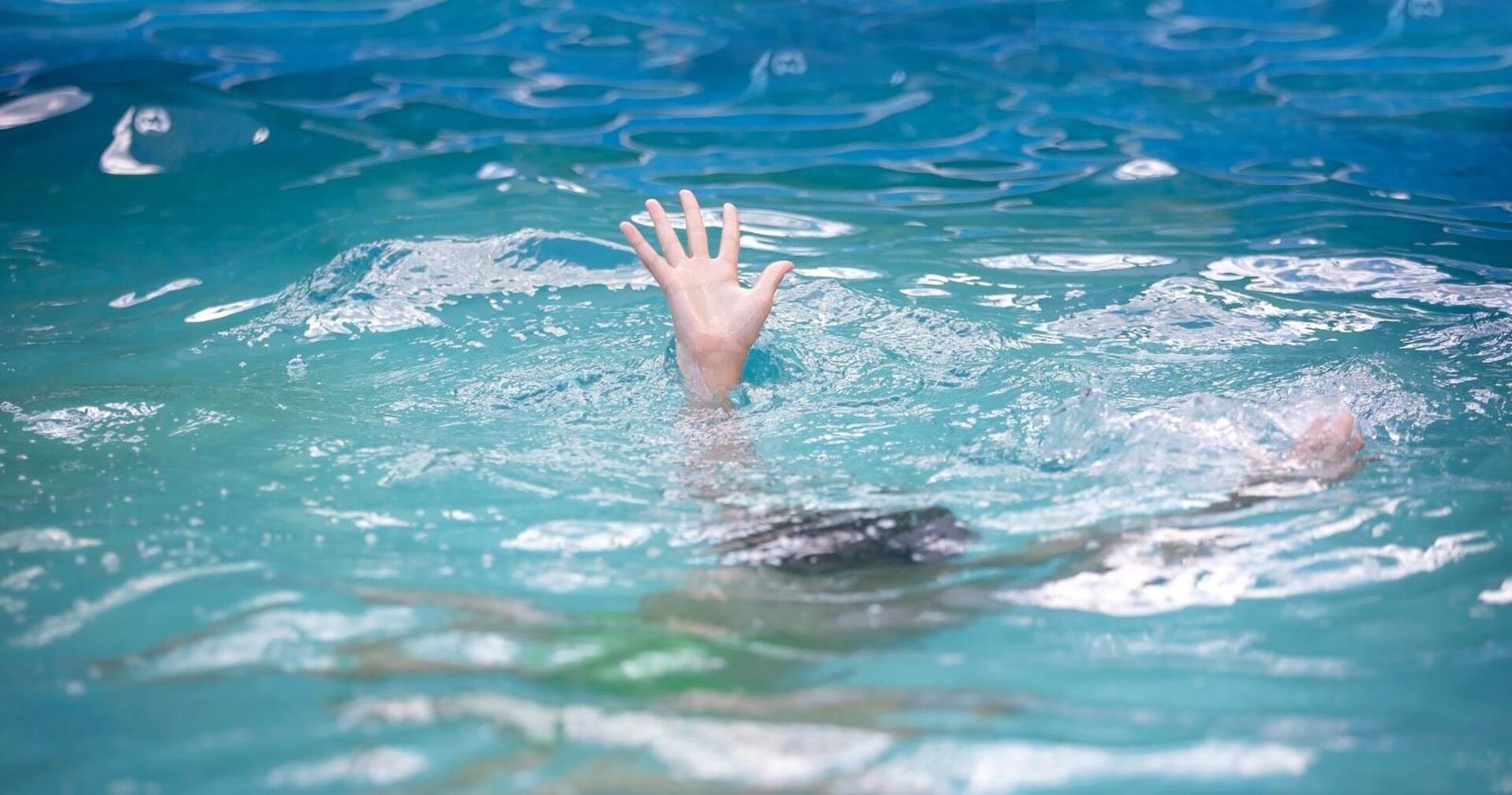 Die Hand eines Kindes schaut aus dem Wasser eines Hallenbads.