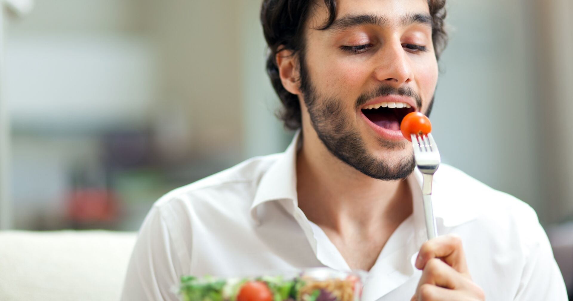 Mann führt eine Tomate mit einer Gabel zum Mund