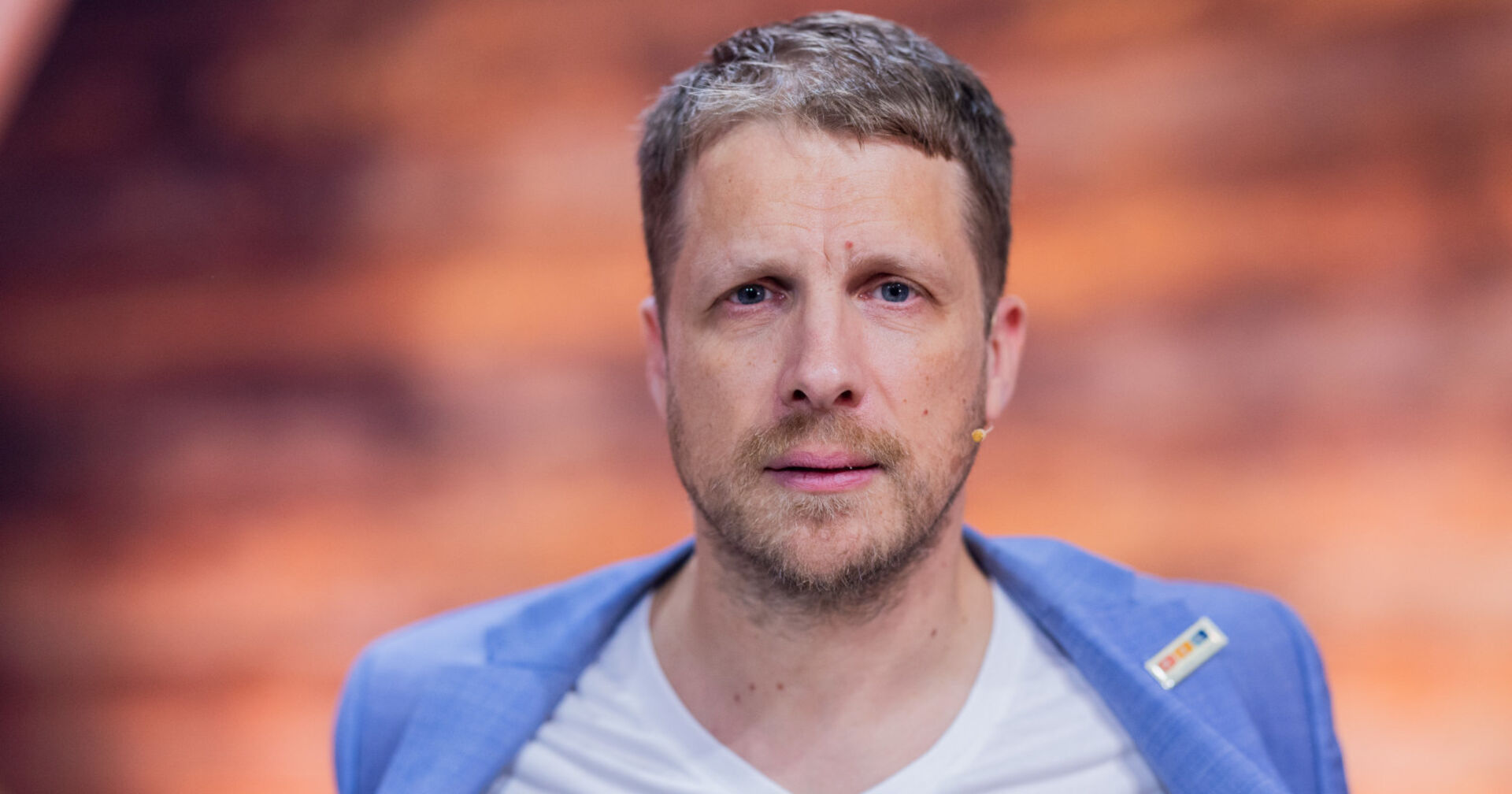 Ein blondhaariger Mann blickt direkt in die Kamera