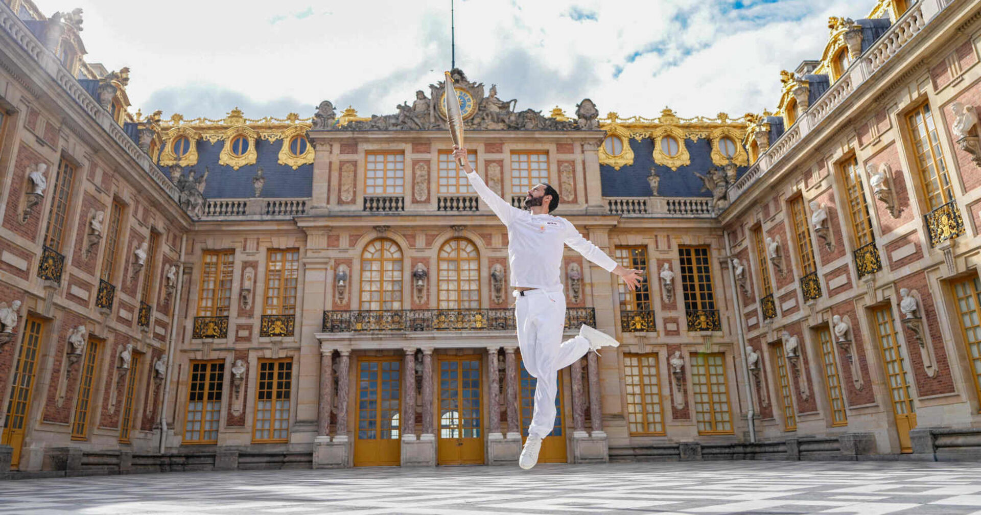 Weiß-angezogener Mann springt vor barockem Gebäude in die Luft