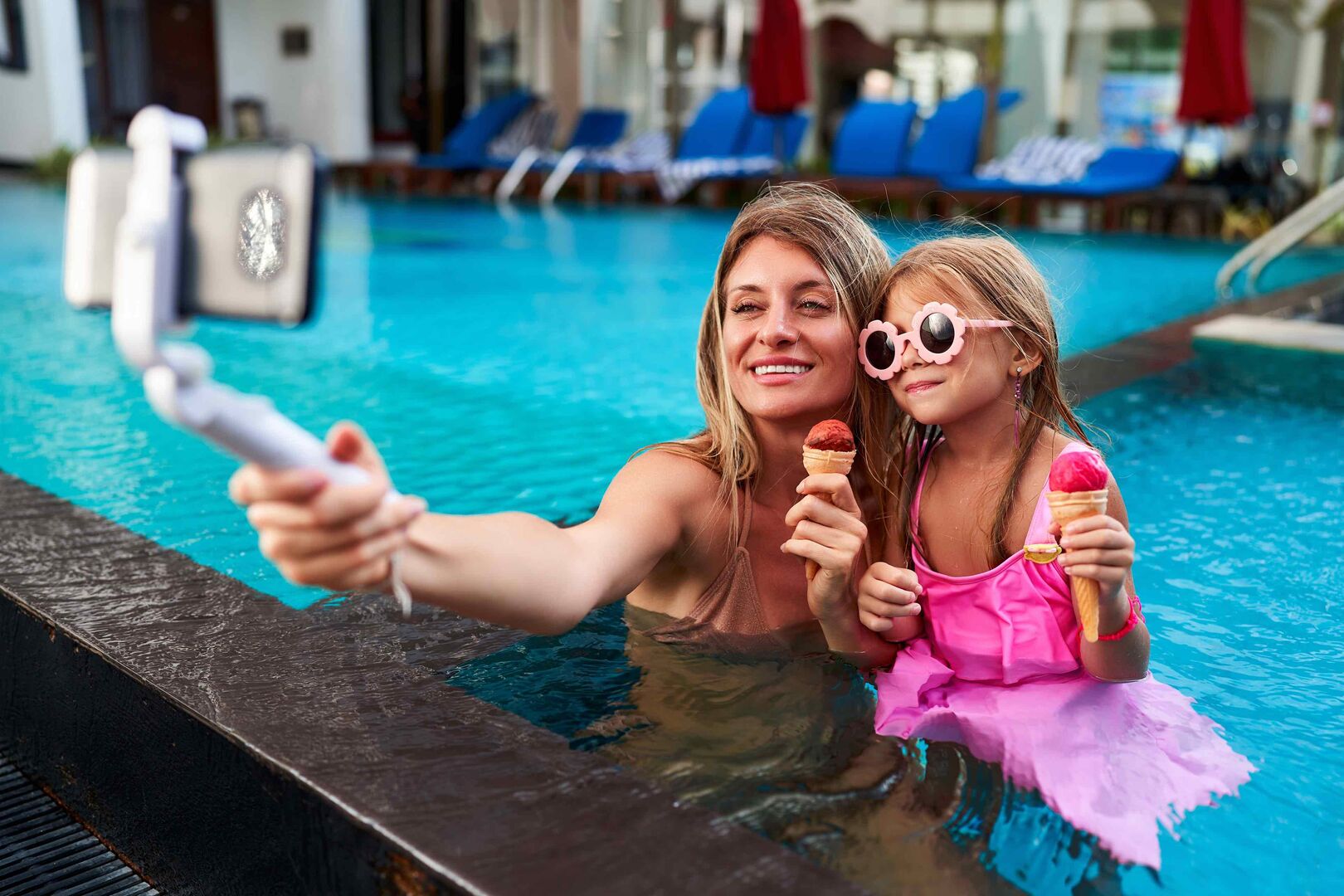 Mutter und Tochter mit Selfie-Stick am Pool