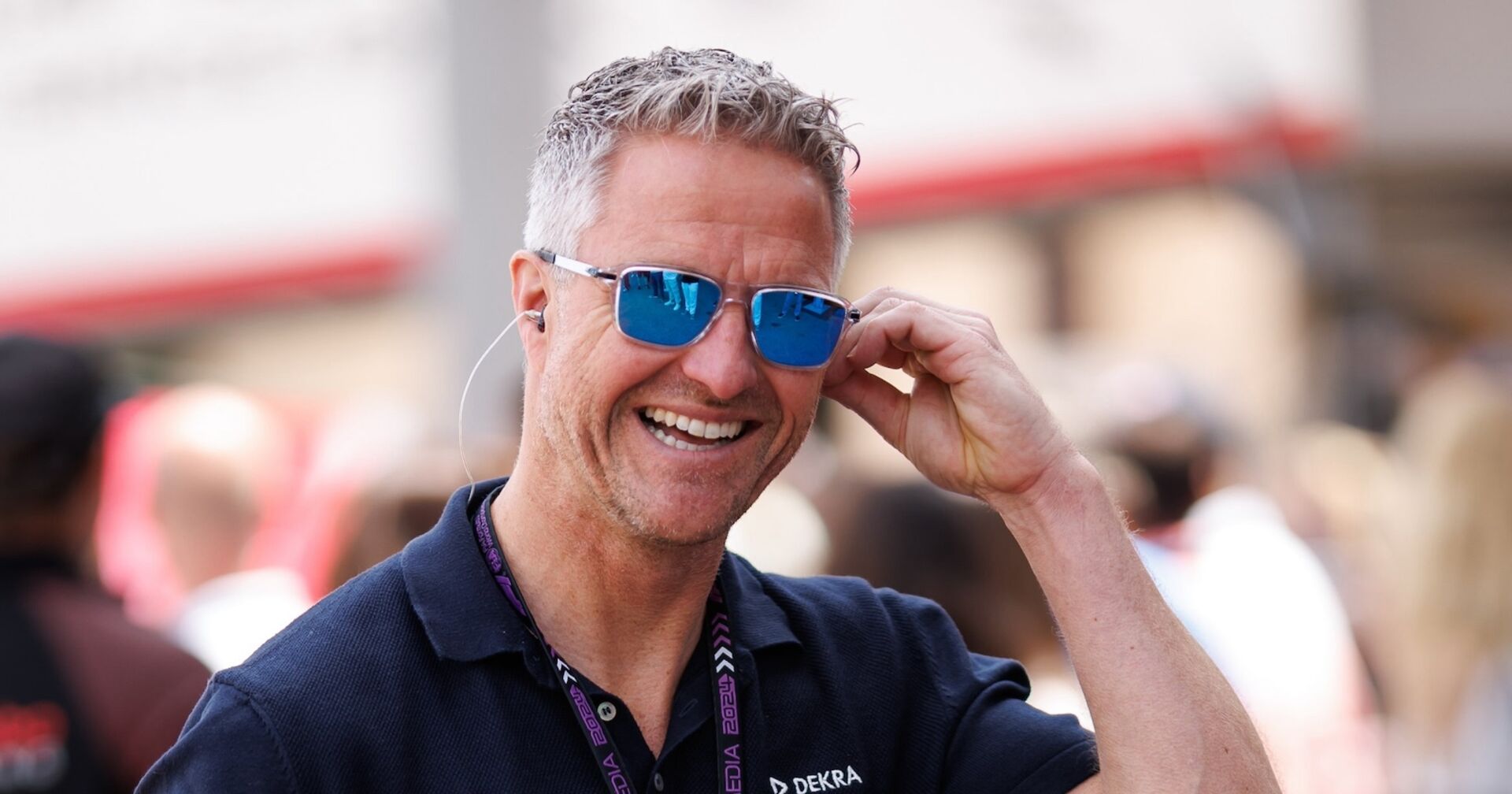 Ralf Schumacher bereit lachend, greift an seine Sonnenbrille