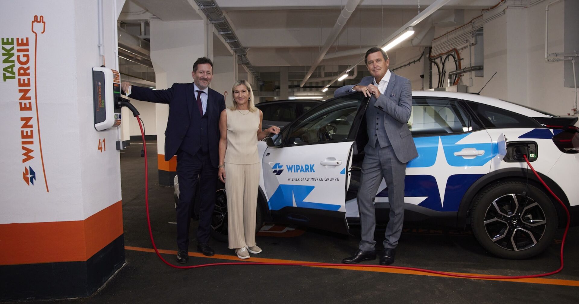 Drei Personen vor einem Auto, bei einer E-Ladestation