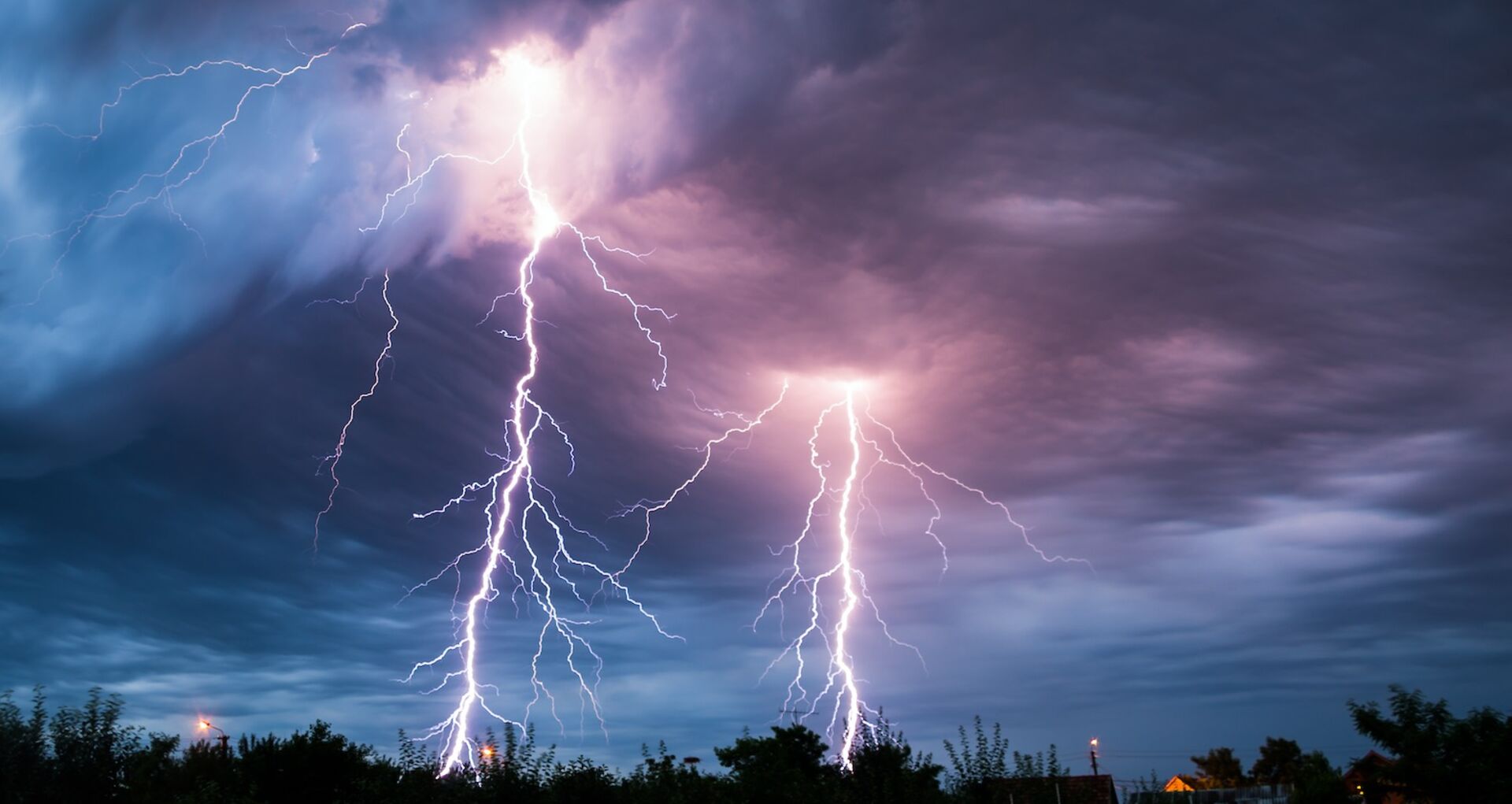Gewitter mit Blitzen über Bäumen und Häusern.