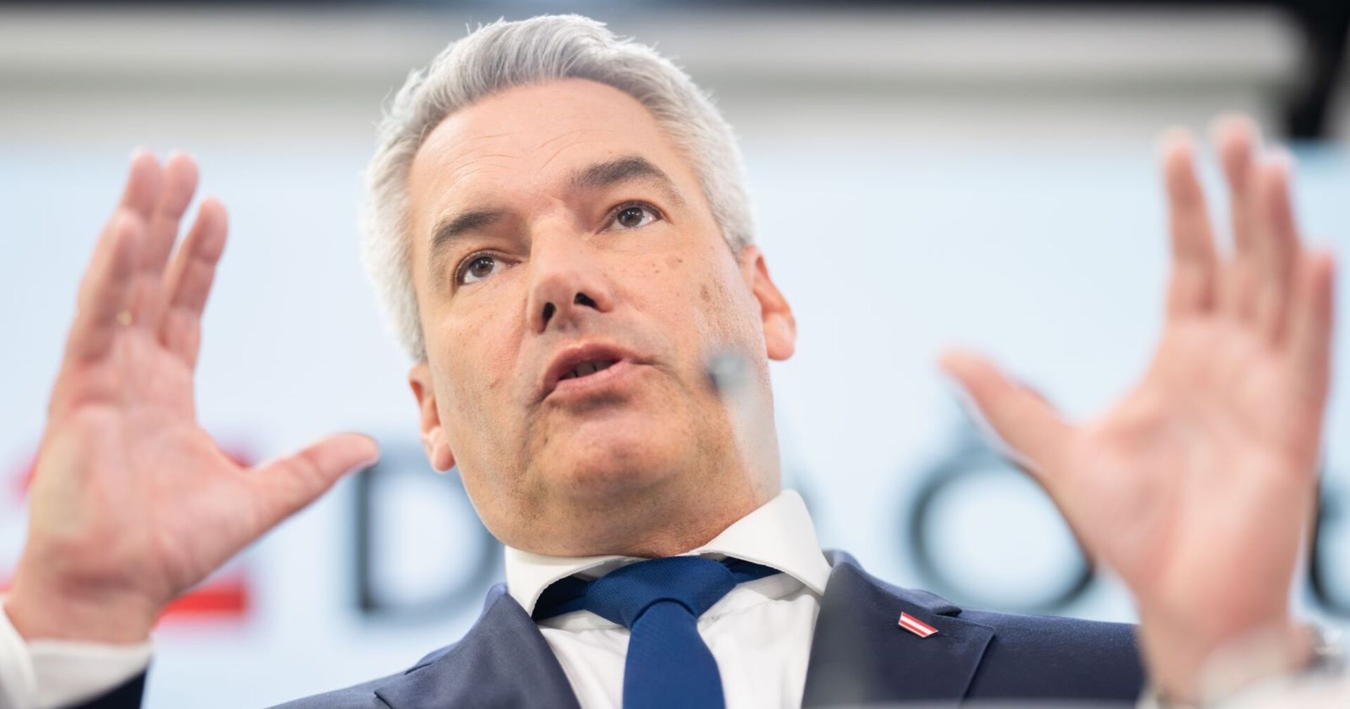 Bundeskanzler Karl Nehammer steht auf einer Bühne mit ausgestreckten Händen