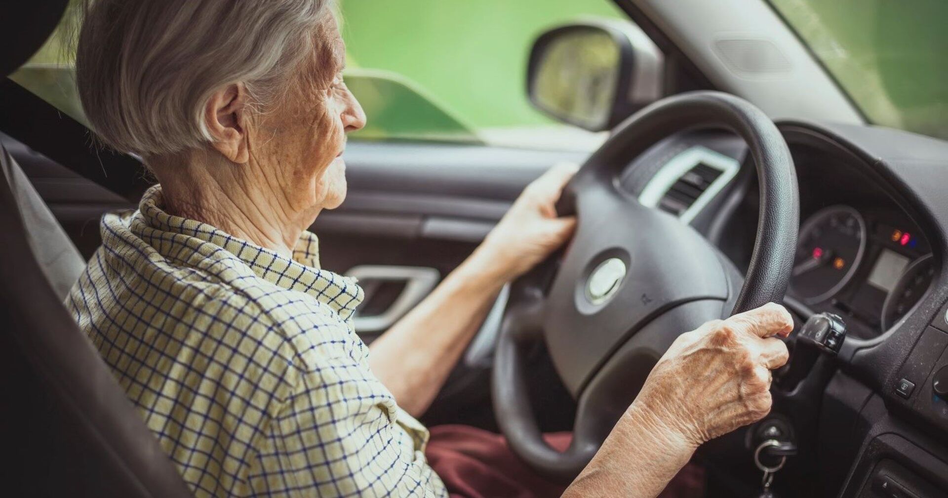 Ein alte Frau sitzt hinter dem Steuer eines Pkw.