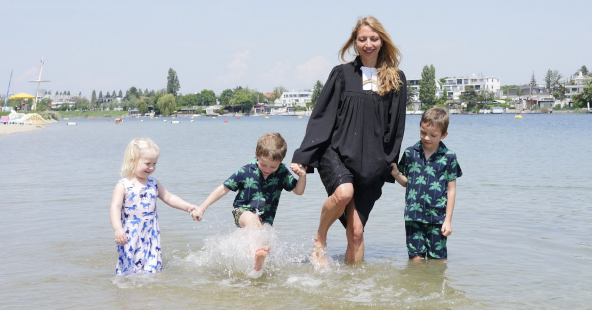 Pfarrerin steht im Talar und drei Kindern im Wasser