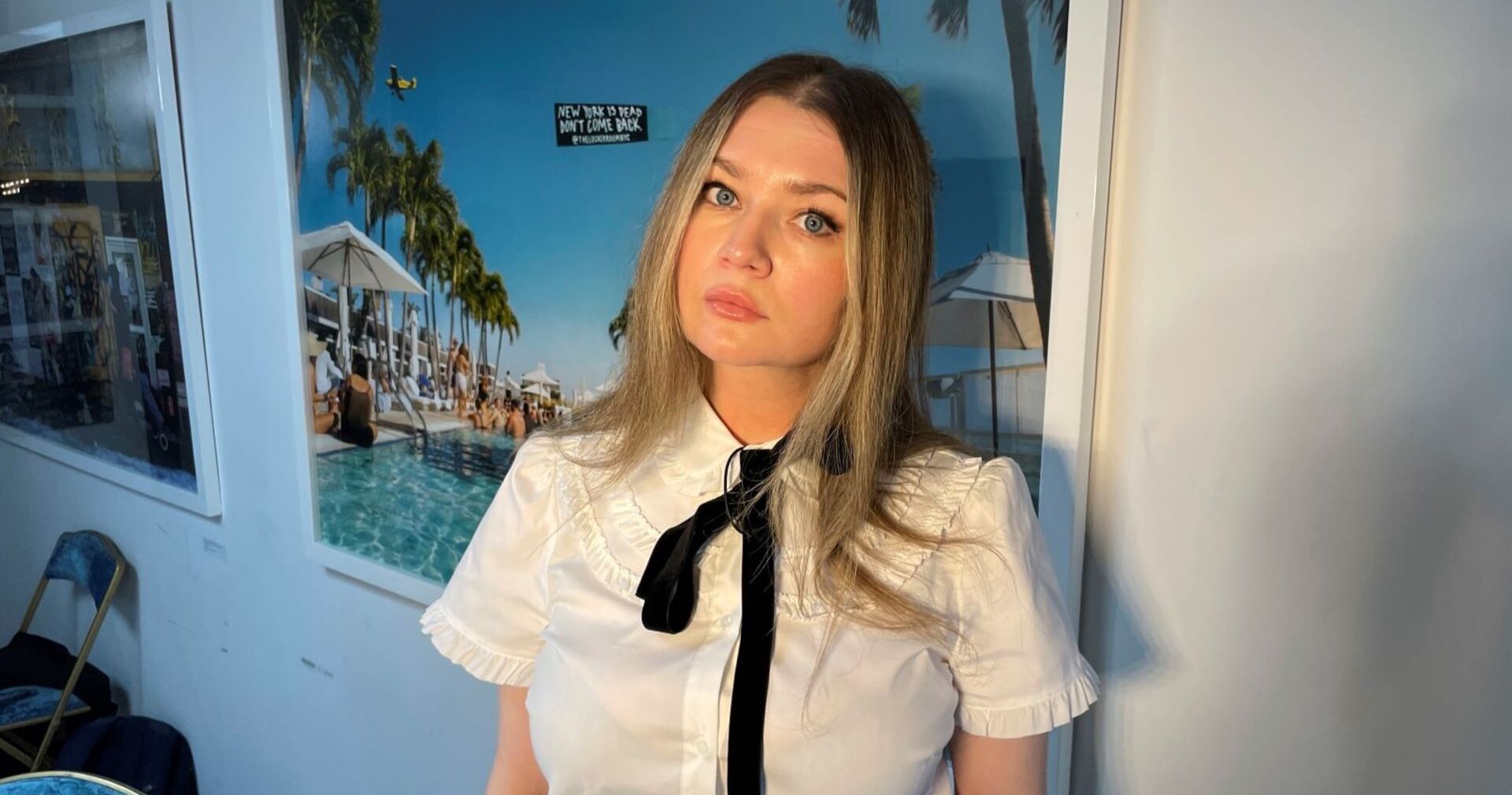 Anna Sorokin steht beim Dreh ihres Podcasts vor einem Urlaubsposter an der Wand