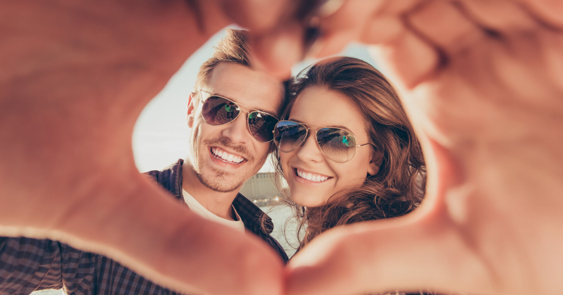 Mann und Frau zeigen mit den Händen ein Herz und lächeln in die Kamera