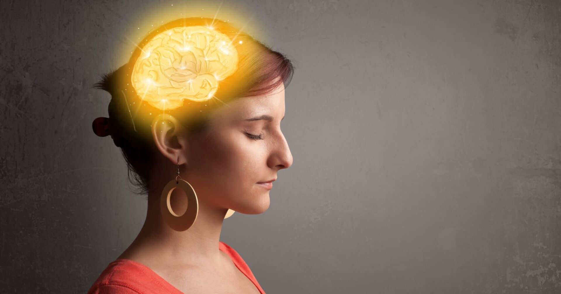 Eine Frau mit mittellangen braunen Haaren hat die Augen geschlossen. Sie konzentriert sich. Sie trägt große braune Ohrringe und einen roten Pulli. Im Kopf der Frau ist ein leuchtendes Gehirn zu sehen.