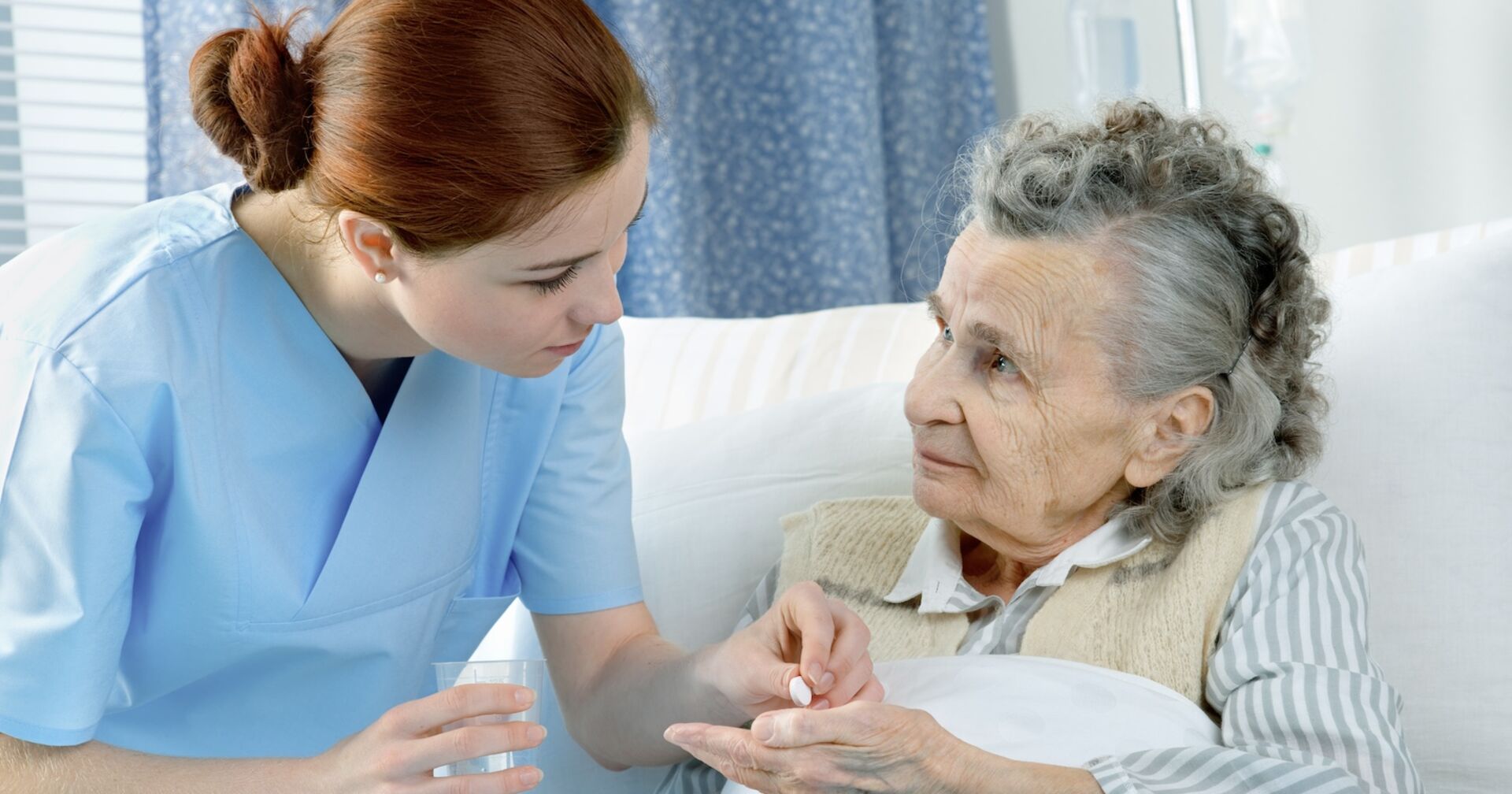 Junge Pflegerin gibt alter Dame ein Medikament in die Hand