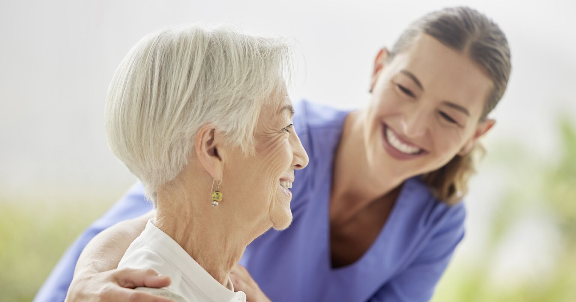 Junge Pflegerin kümmert sich um gut gelaunte, ältere Dame