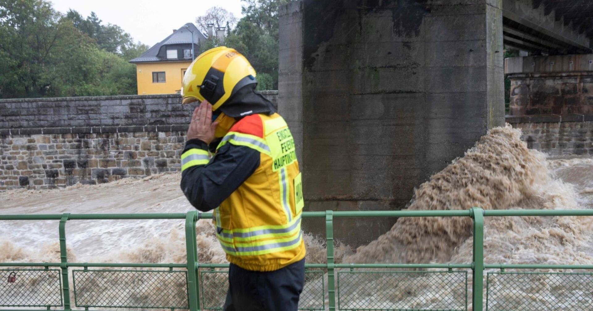Ein Feuerwehrmann telefoniert, hinter ihm der reißende Wienfluss