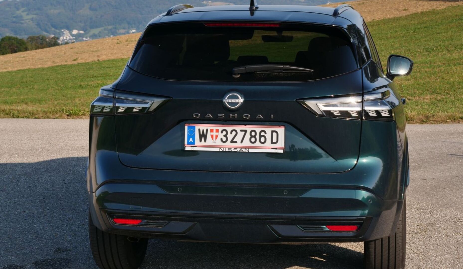 Der neue Nissan Qashqai. Das dunkelgrüne Auto glänzt in der Sonne. Im Hintergrund ist eine Wiese zu sehen.