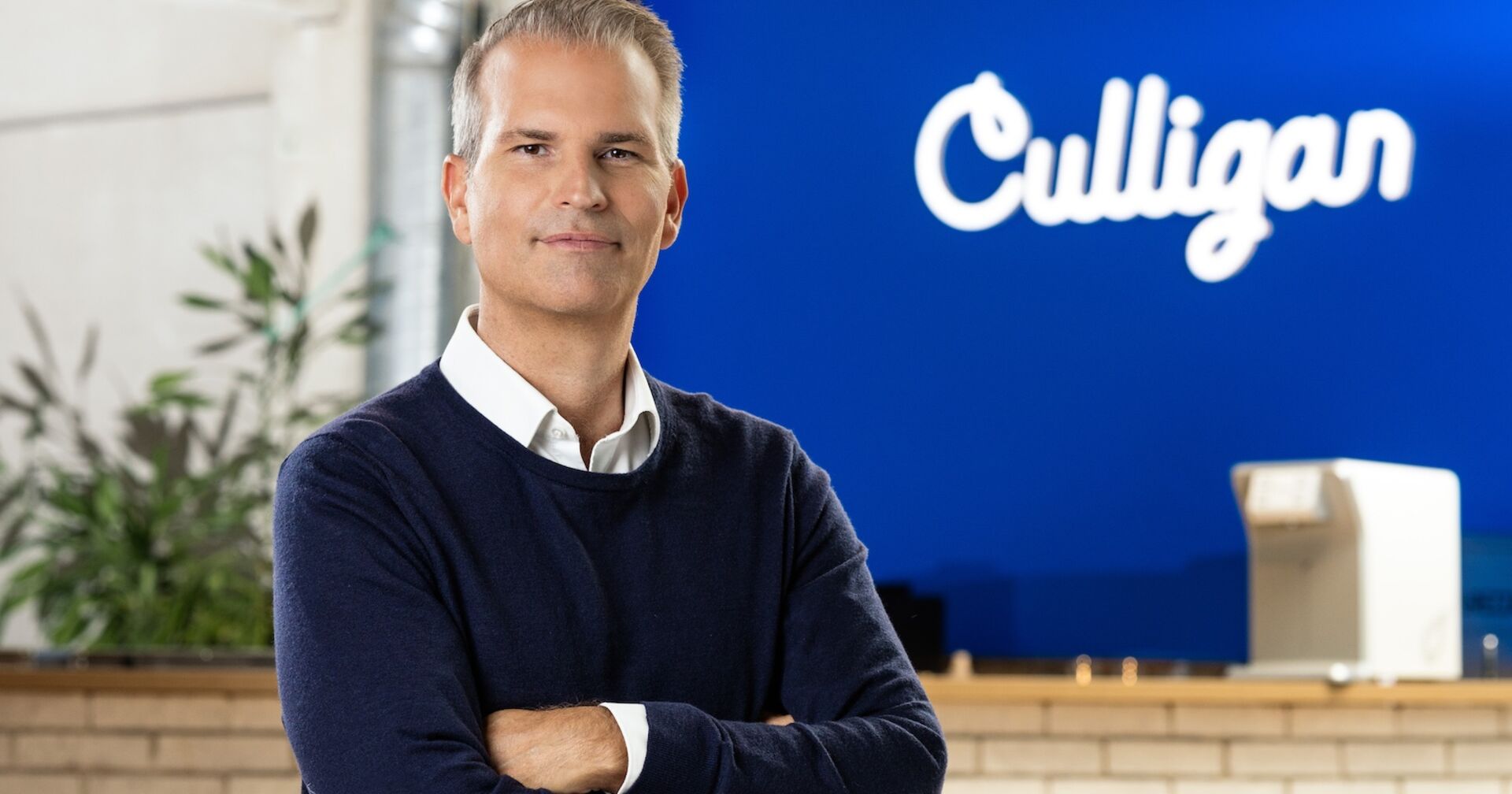 Mann mit weißem Hemd und dunkelblauem Pullover verschränkt die Hände