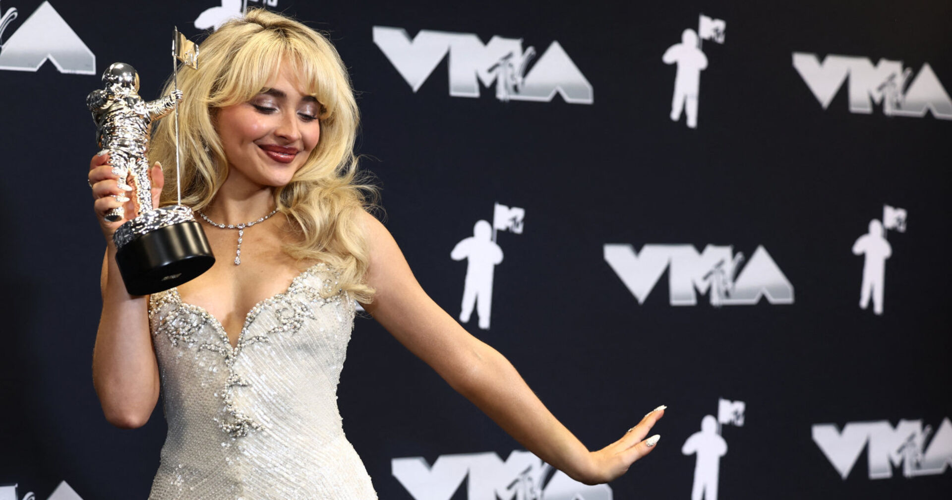 Eine blonde Frau im Glitzerkleid hält eine Trophäe in der Hand