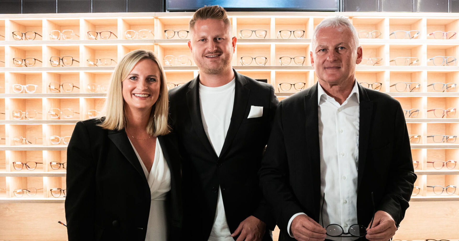 Zwei Männer und eine Frau stehen vor einem Brillenregal