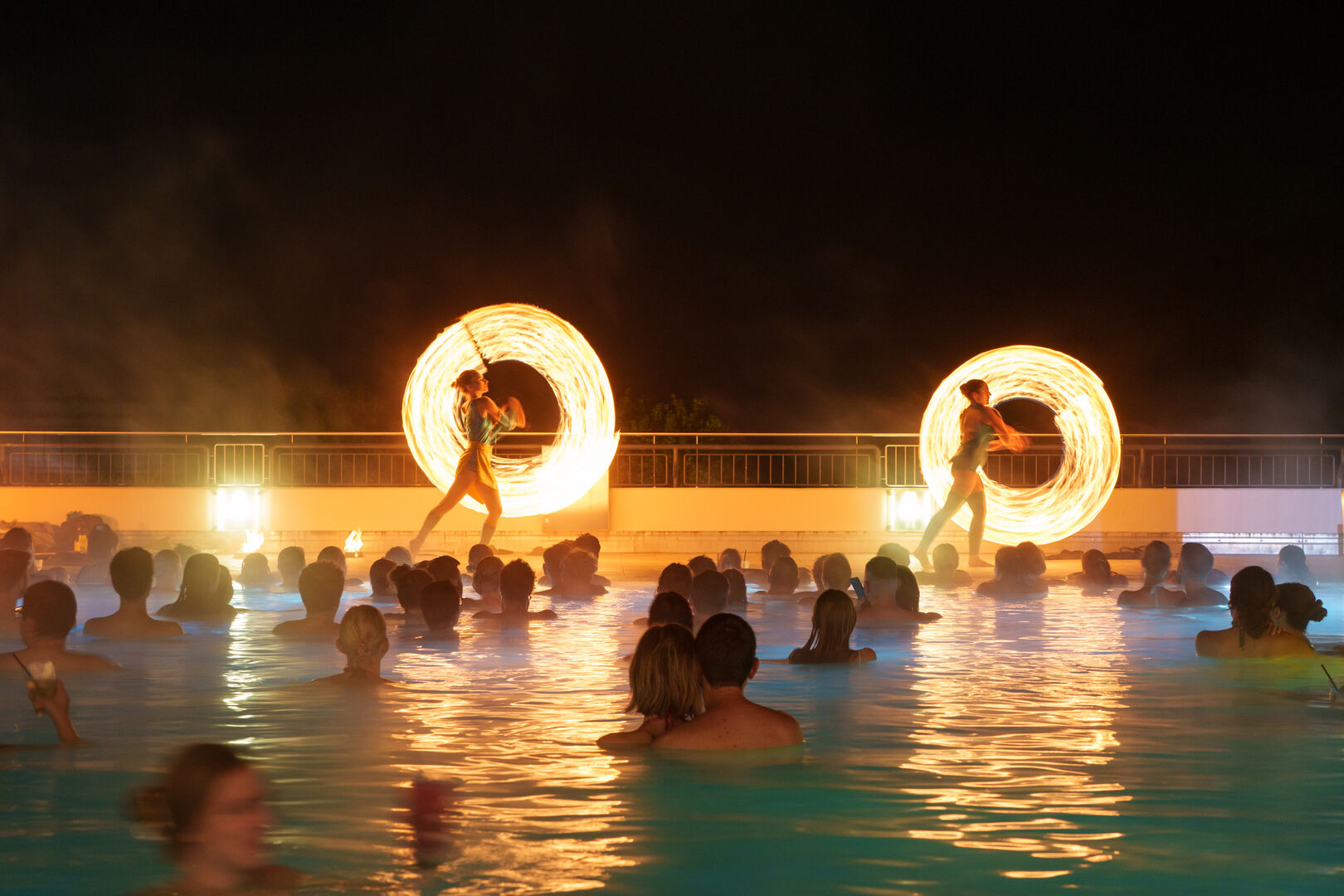 Zwei Frauen hantieren mit Feuer vor einem Schwimmbad