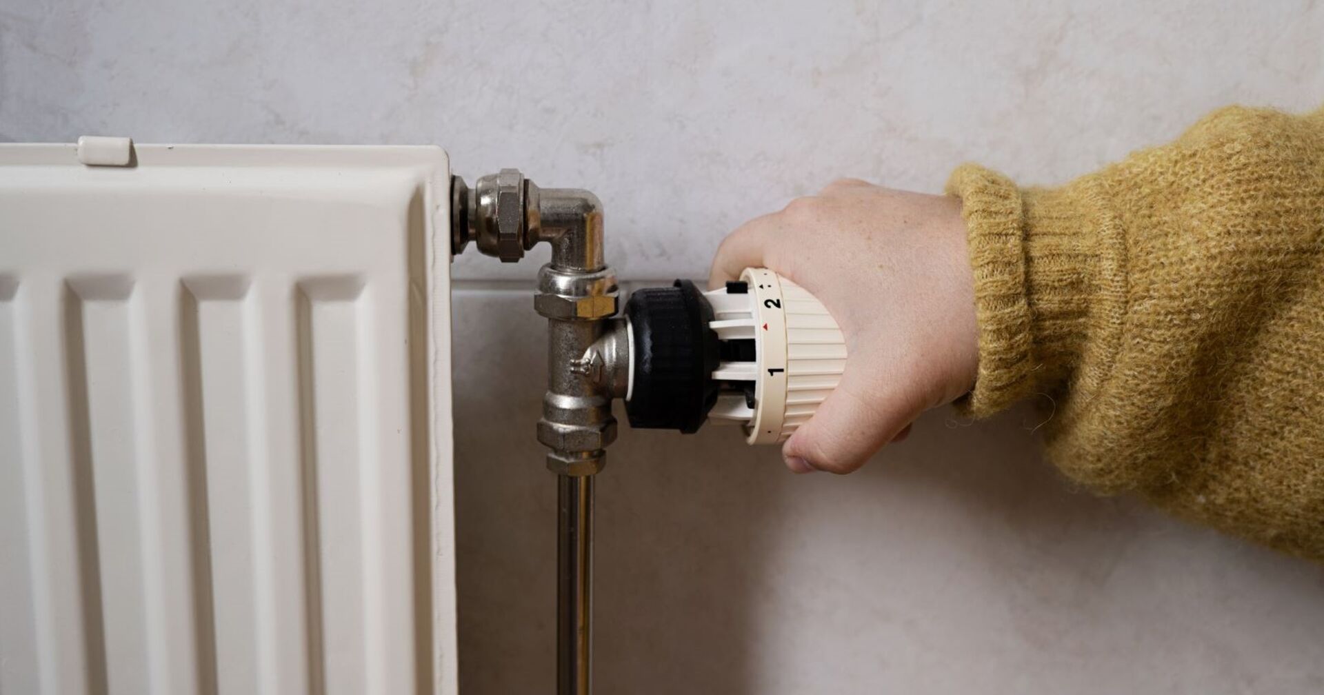 Eine Hand regelt die Temperatur an einem alten Heizkörper.