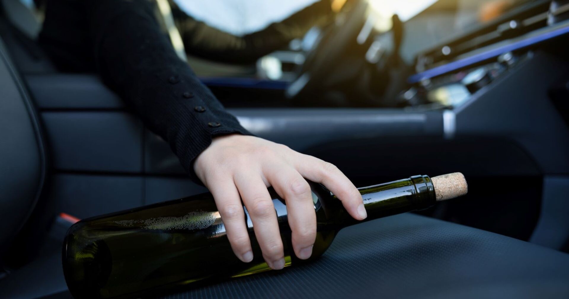 Eine Frau hinterm Steuer mit einer Weinflasche am Beifahrersitz.