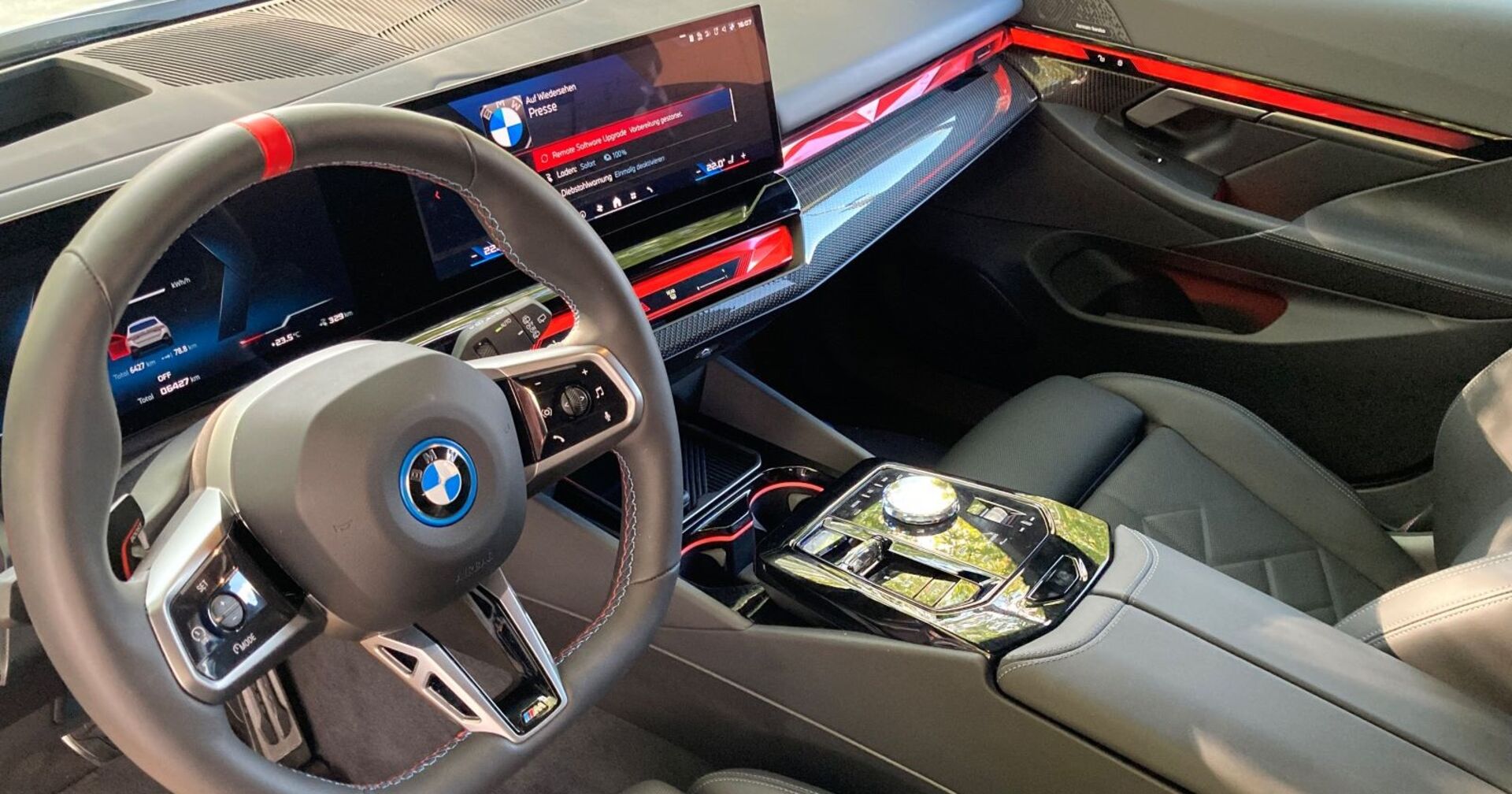 Das Innenleben des BMW i5 M60 xDrive: iDrive-Schalter sowie Fahrerlebnisschalter laden zum Genuss ein. Lenkrad und Mittelkonsole sind in einem hellen grau gehalten, rote Linie geben dem Innenleben den gewissen Kick.