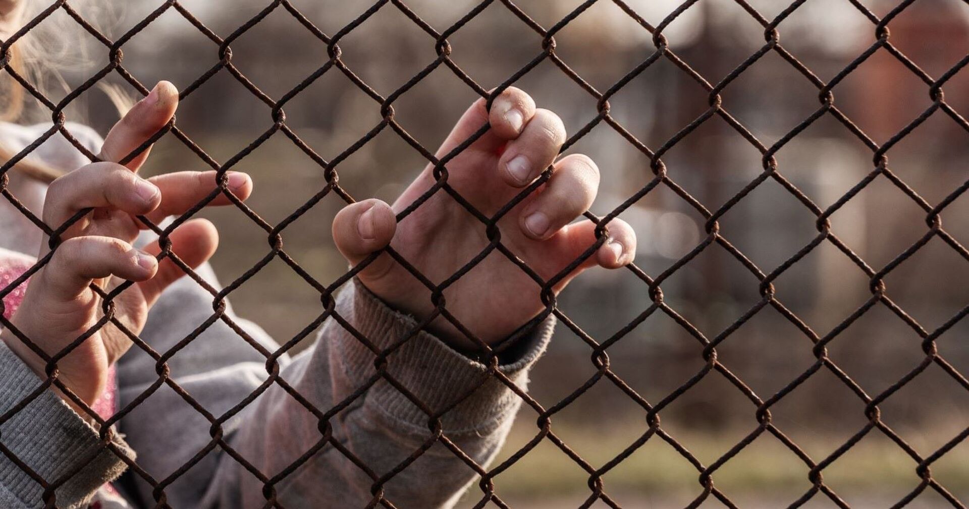 Kinderhände an einem Metallzaun.