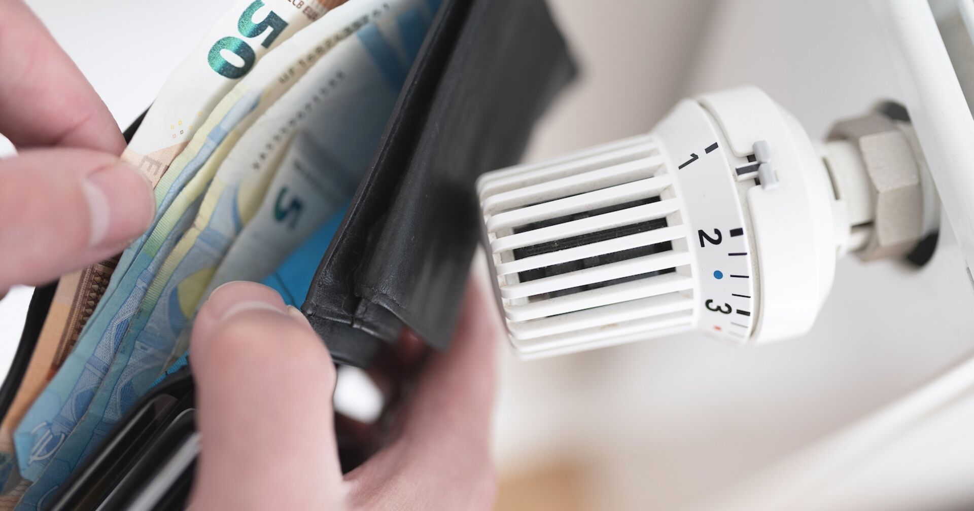 Jemand schaut neben einer Heizung in seine Geldbörse.