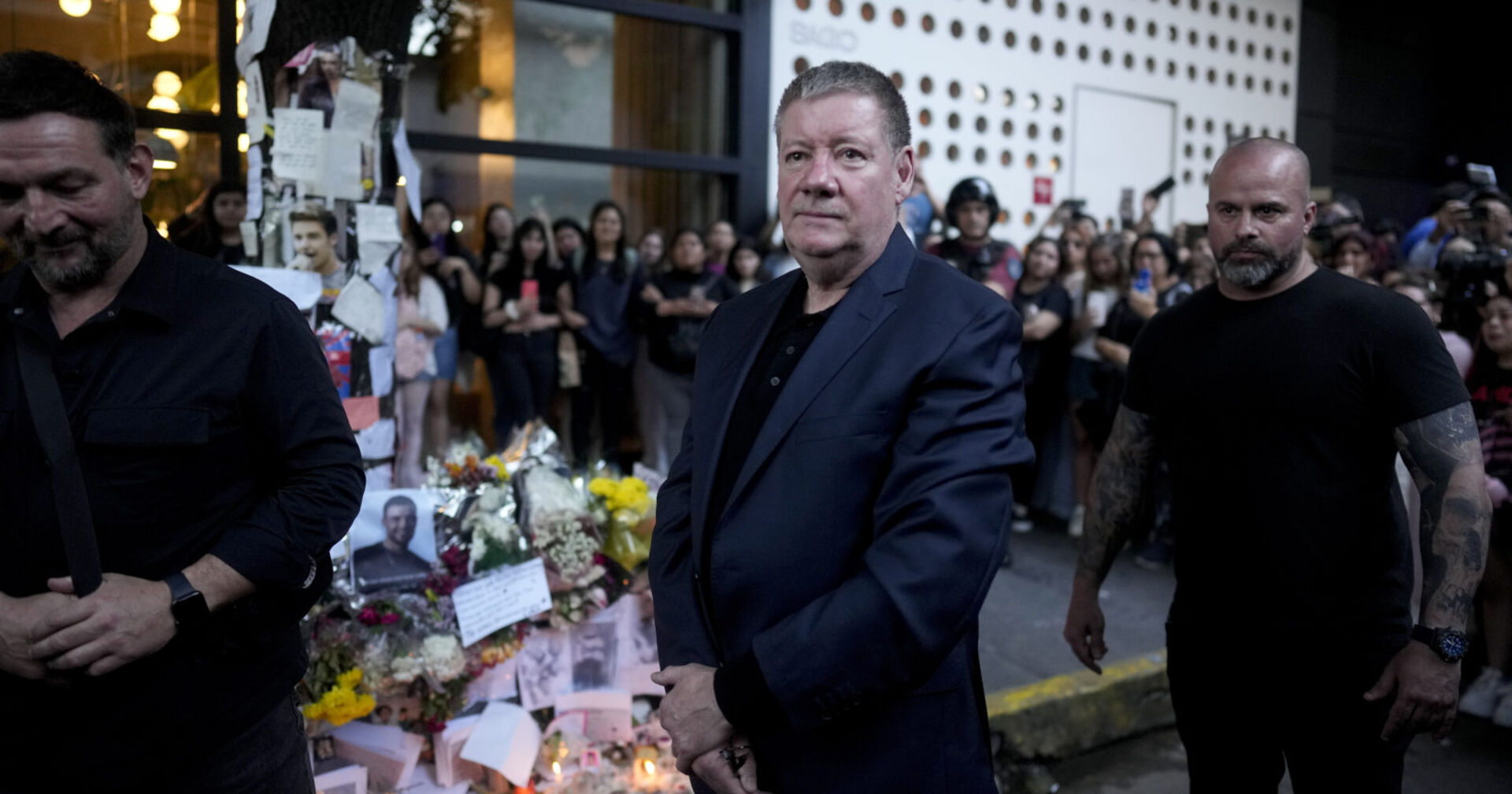 Ein Mann steht vor einer Gedenkstätte und mehreren Fans