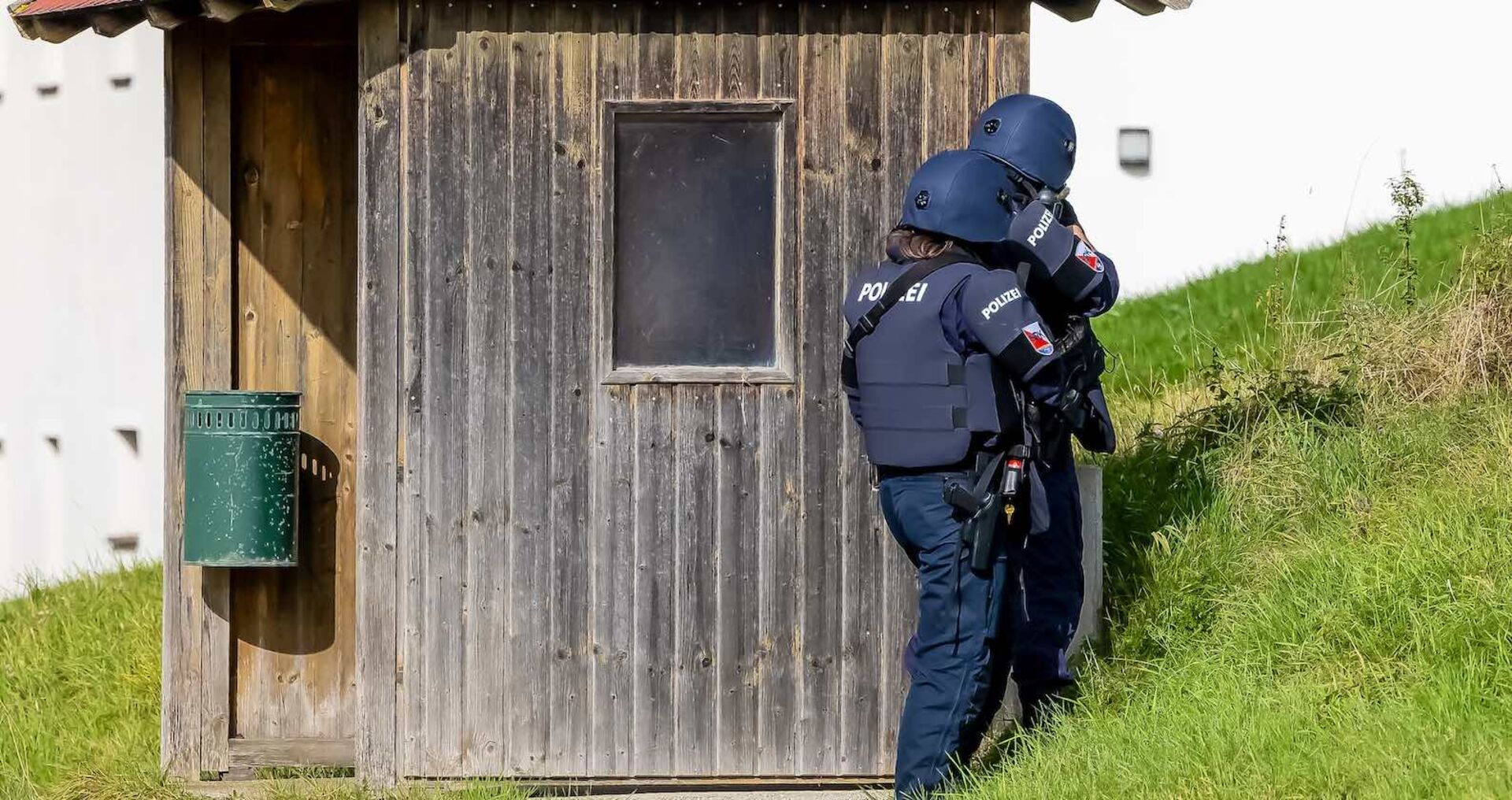 Zwei Polizeibeamten hinter einem Holzhäuschen.
