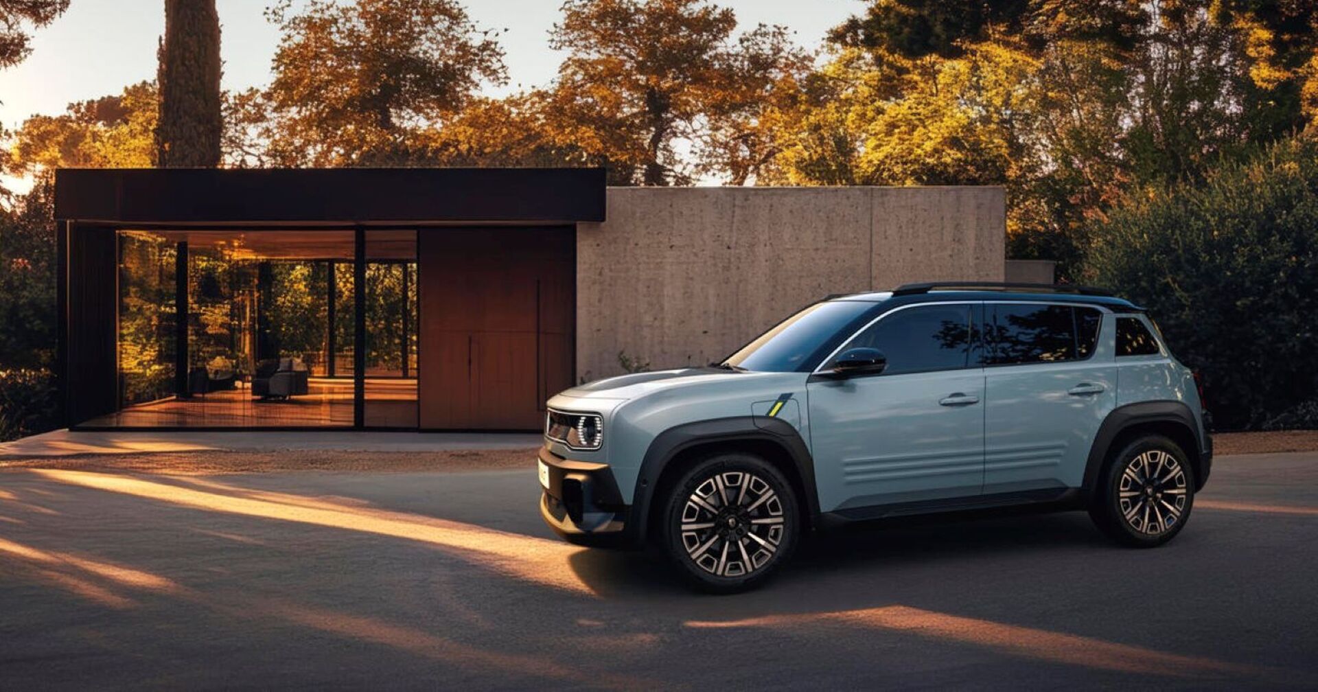 Ein hellblauer Renault RV parkt vor einem modernen Haus. Man sieht einen Glaseingang und hinter dem Haus wachsen zahlreiche hohe Laubbäume.