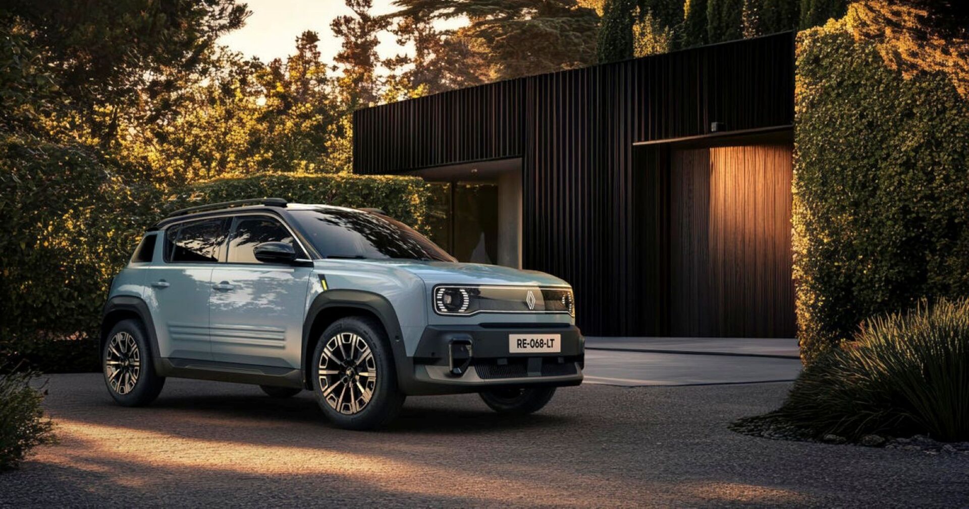 Der Renault R4 in einem sehr hellen blau steht auf einen bewaldeten Parkplatz. Die Sonne beleuchtet das Auto nur schwach. Im Hintergrund sieht man eine modernes braunes Haus inklusive Garage.