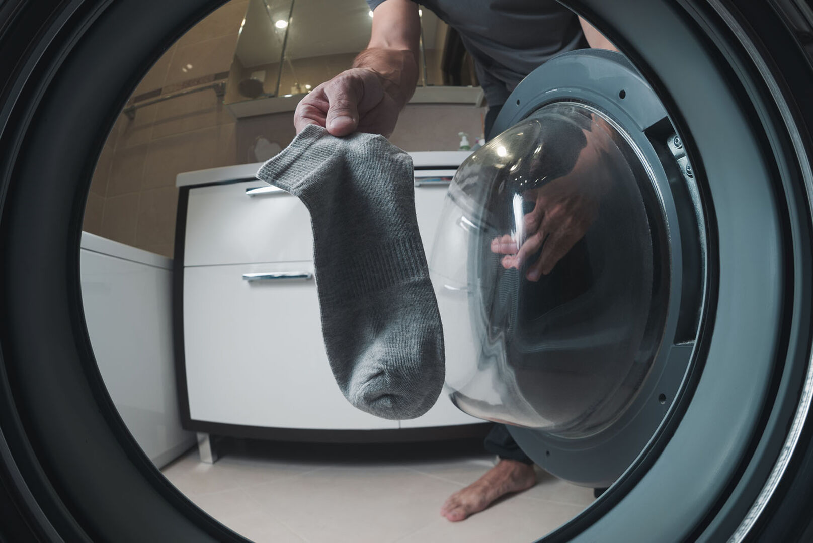 Mann gibt Socken in Waschmaschine | Credit: iStock.com/happyphoton