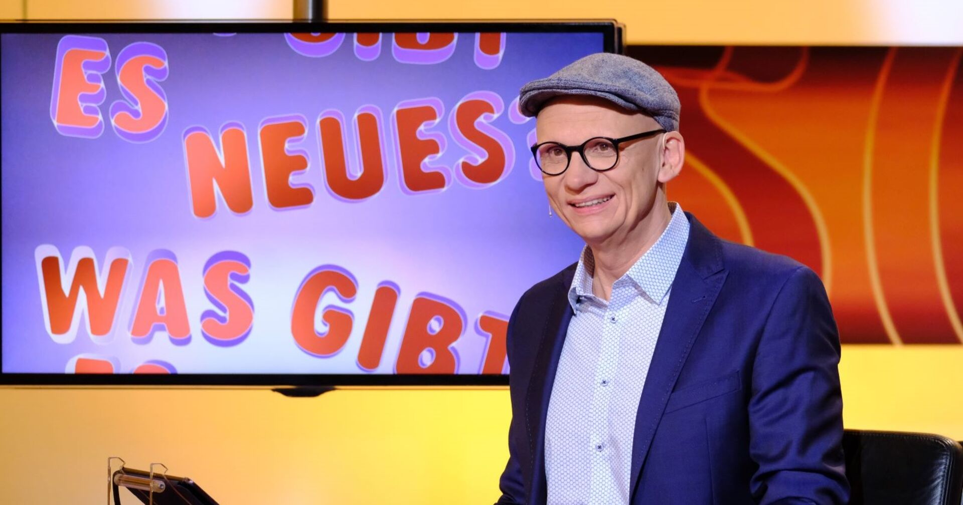 Moderator Baier sitzt vor einem Bildschirm.