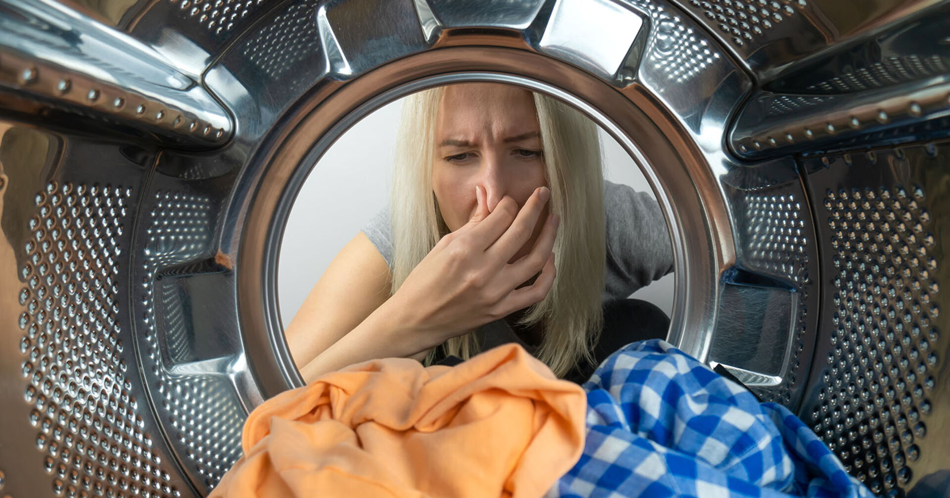 Frau nimmt stinkende Wäsche aus der Waschmaschine | Credit: iStock.com/Olga Ihnatsyeva