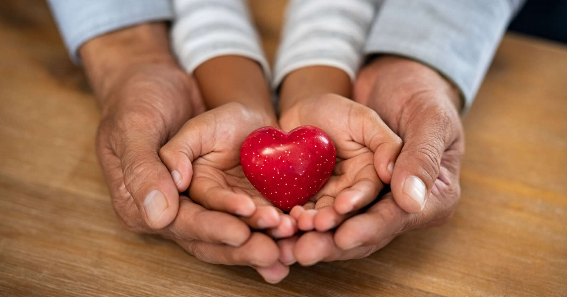 Vier Hände halten ein Herz aus Stein in den Händen