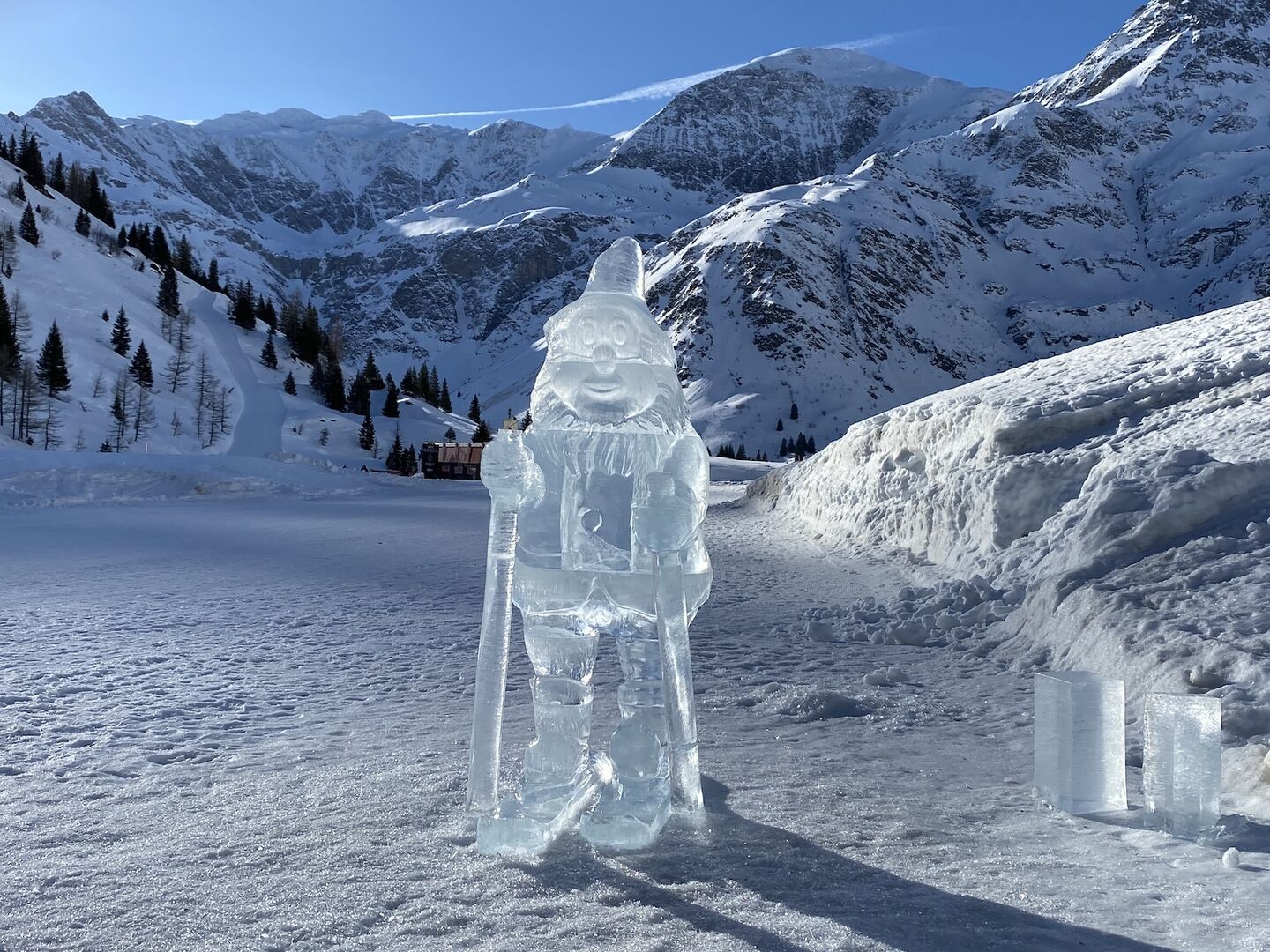 Zwerg aus Eis steht auf der Piste, dahinter Bergwelt