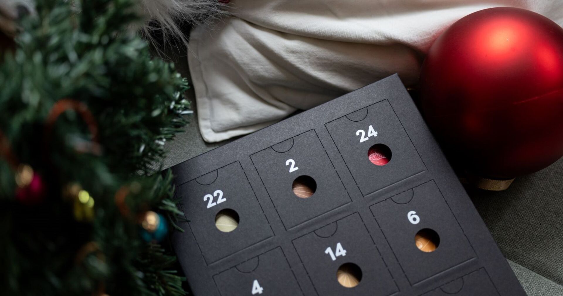 Ein Adventkalender liegt neben einer roten Christbaumkugel.