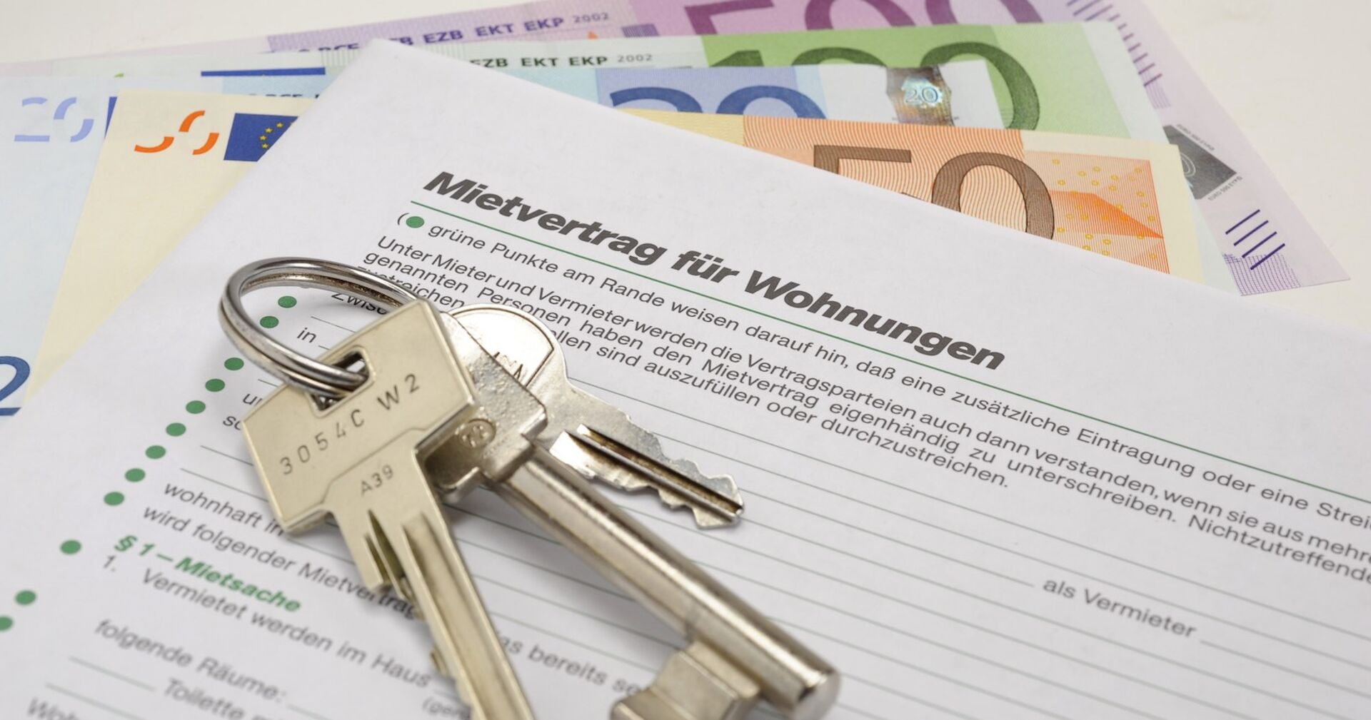 Geld, ein Schlüsselbund und ein Mietvertrag auf einem Tisch.