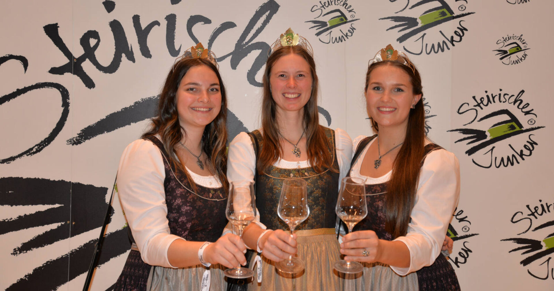 Drei Mädchen im Dirndl stoßen mit Weingläsern an