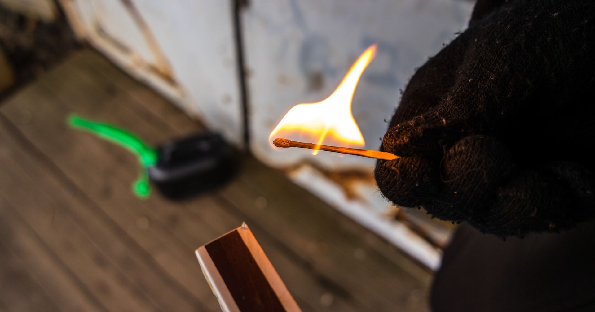 Jemand zündet ein Streichholz, auf dem Boden steht ein Kanister.