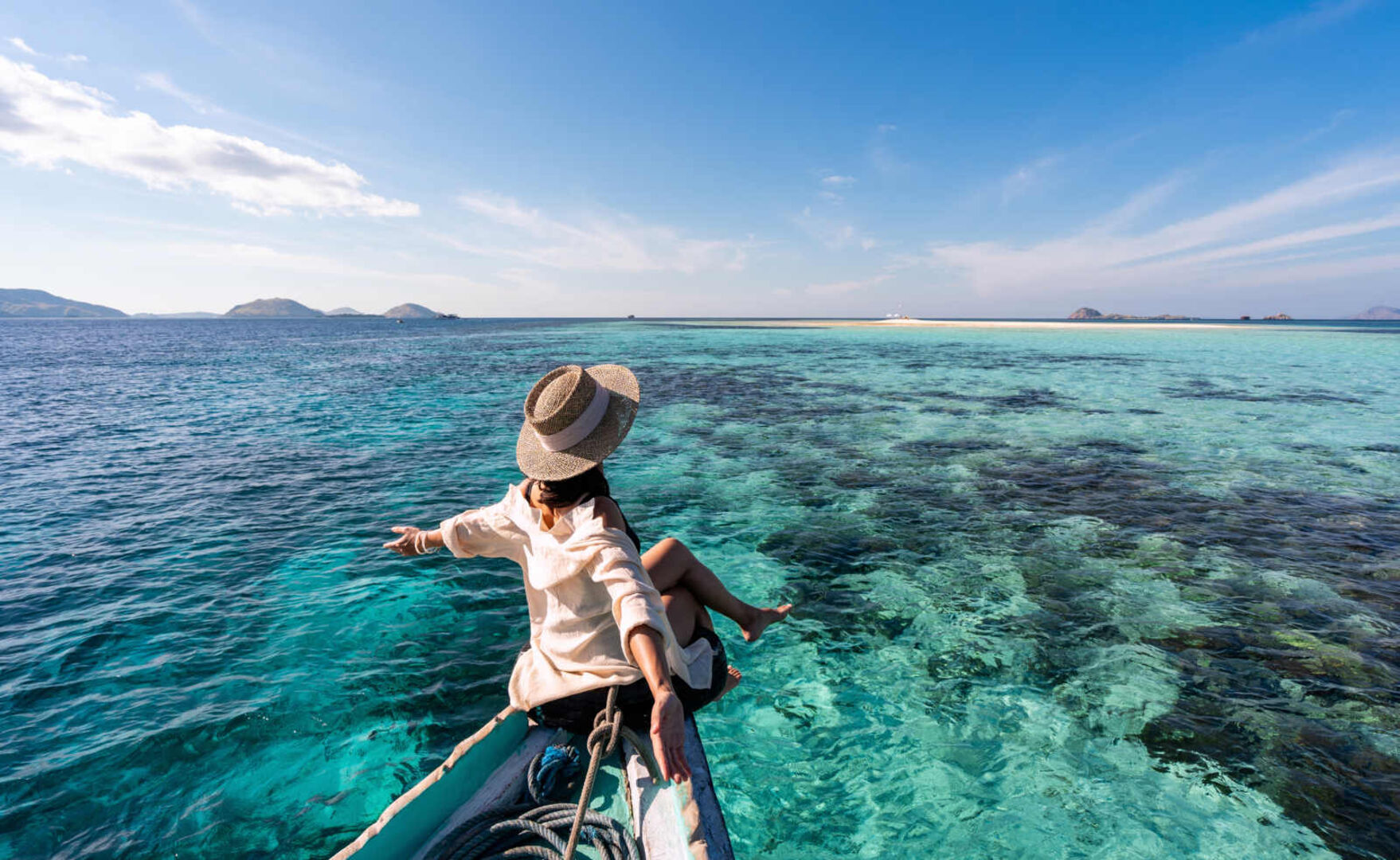 Frau sitzt auf dem Bug eines Bootes und streckt ihre Arme über das Meer aus