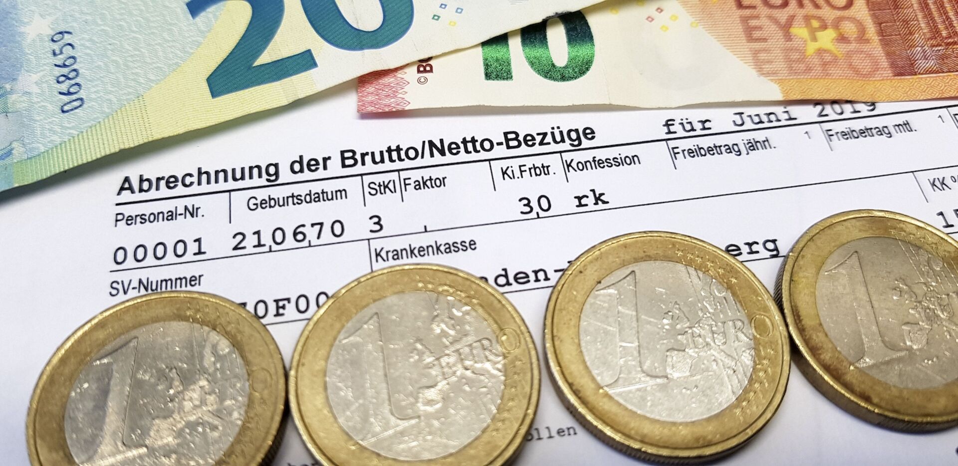 Lohnabrechnung und Euro-Münzen sowie -Scheine.